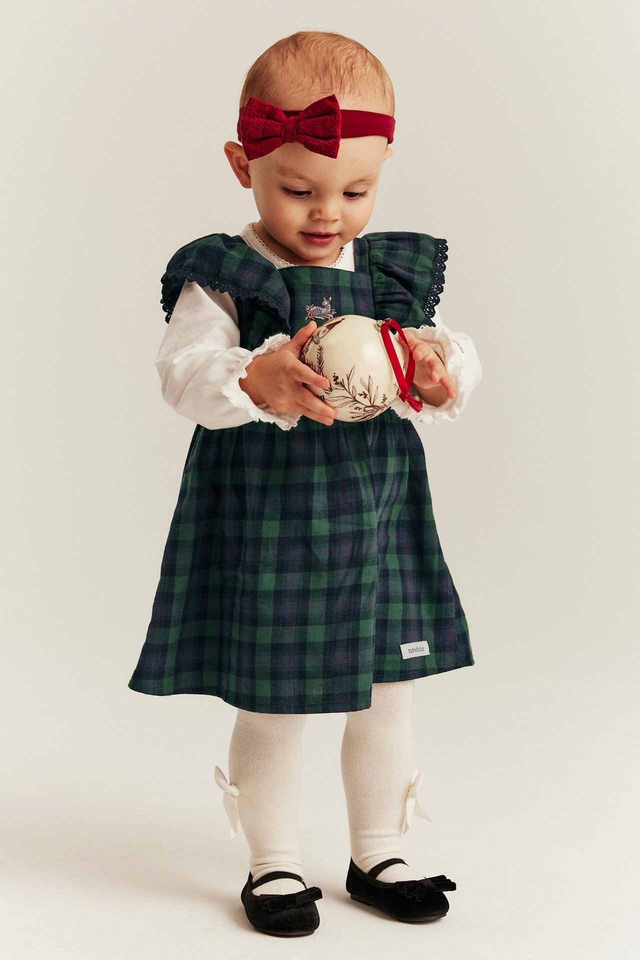 Baby girl in a blue tartan suspender dress with embroidery and lace-trimmed ruffles.