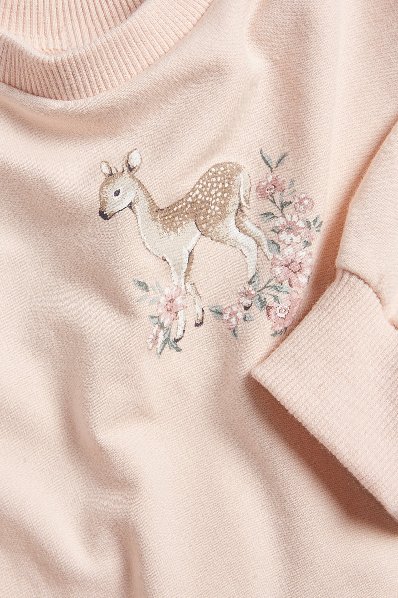 Close-up front view of a light pink sweatshirt with a fawn and floral print on the front.