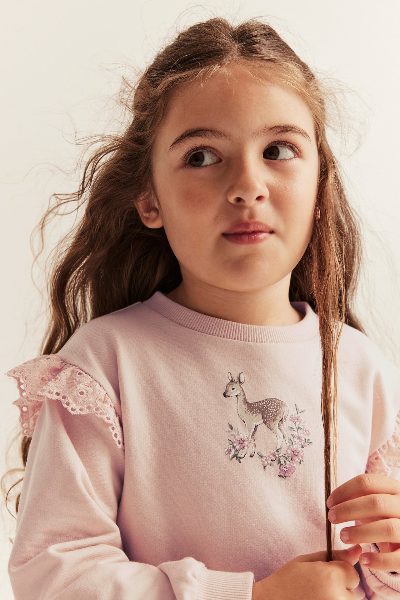 Nahaufnahme von vorne eines Kindes in einem hellrosa Sweatshirt mit Spitzenrüschen und Hirschdruck.