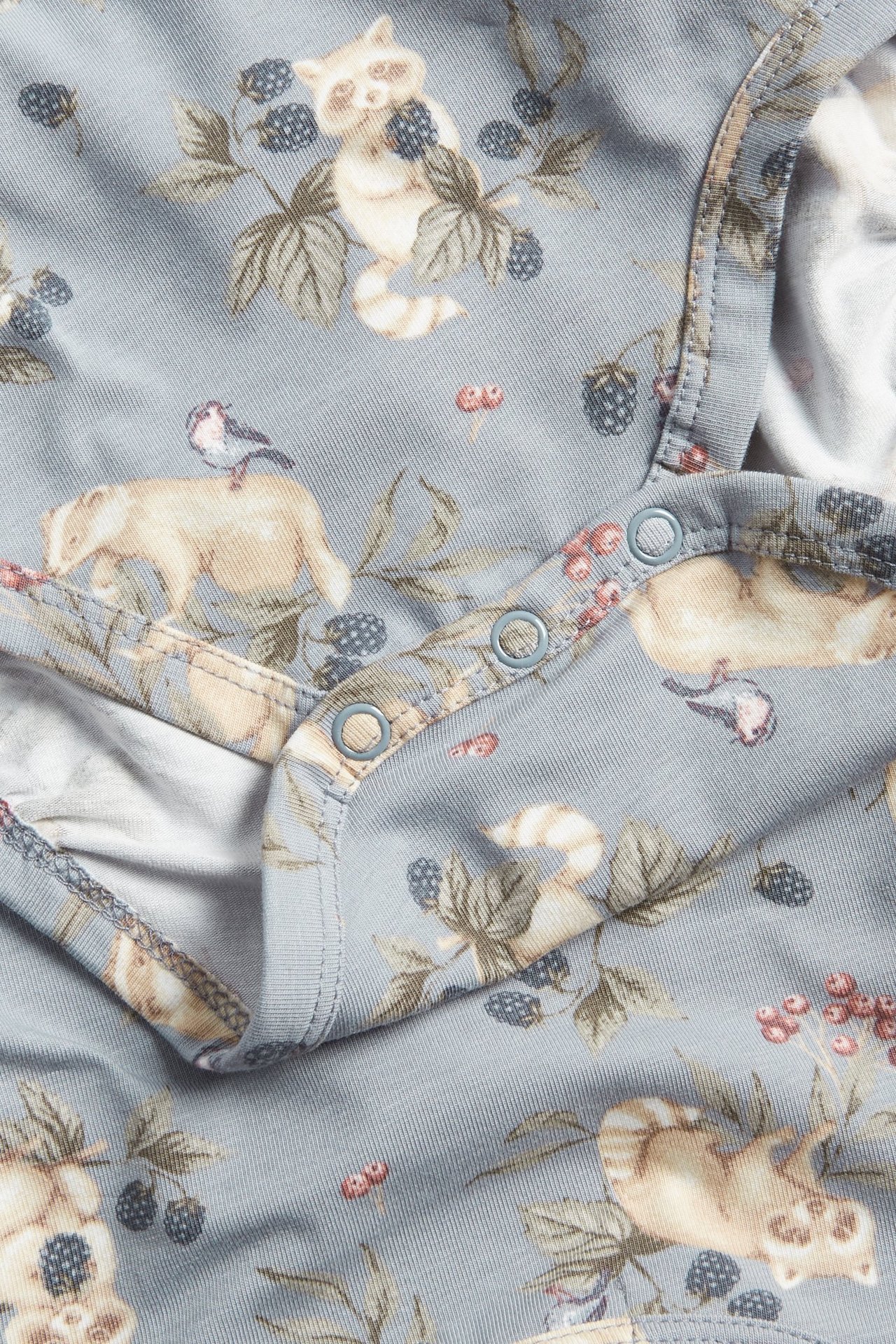Nahaufnahme eines hellblauen Baby-Bodys mit Tier- und Beerenmuster, mit Druckknöpfen.