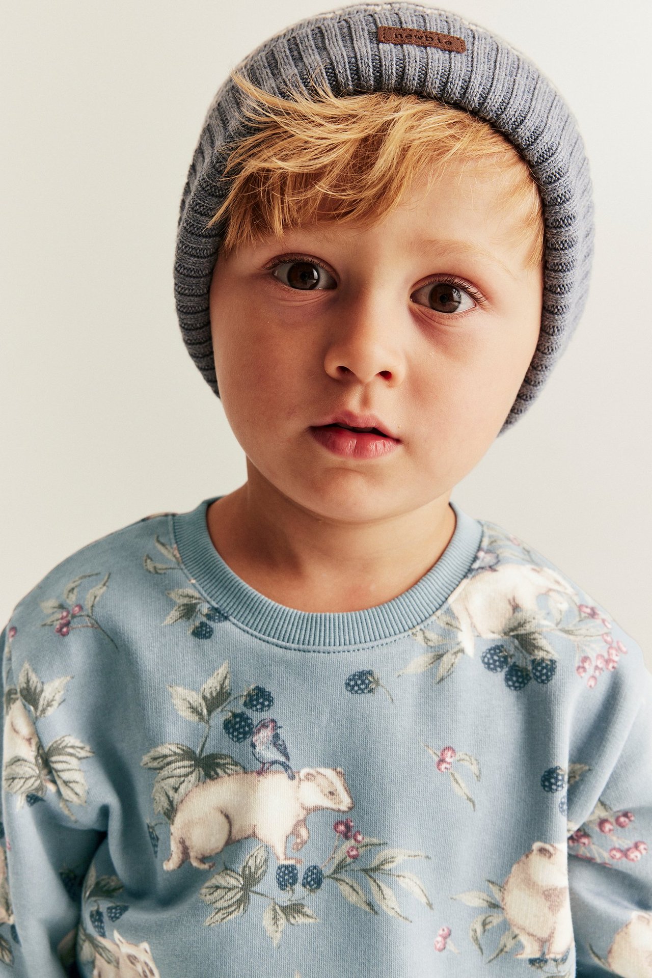 Nahaufnahme von vorne eines Kindes in einem hellblauen Sweatshirt mit Tiermuster und einer grauen Rippmütze.