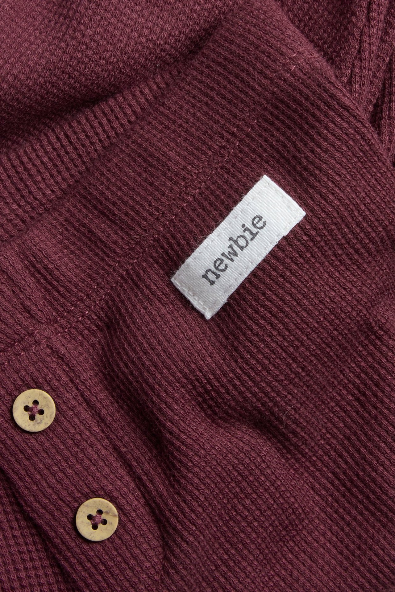 Nahaufnahme weinroter Waffelstrick-Leggings mit zwei dekorativen hellbraunen Knöpfen vorne.