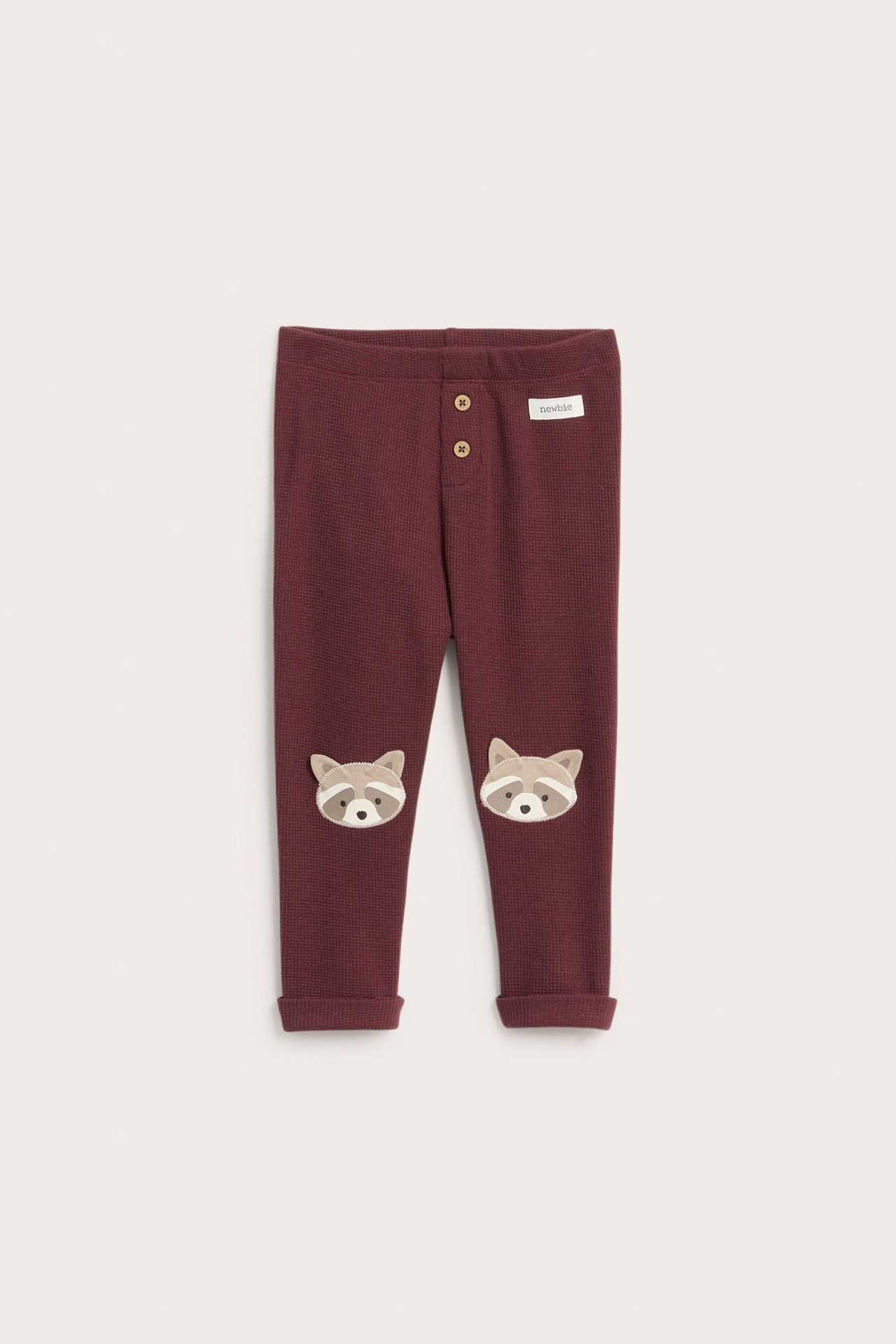 Vorderansicht von weinroten Waffelstrick-Leggings für Kinder mit Zierknöpfen und Waschbär-Applikationen an den Knien.