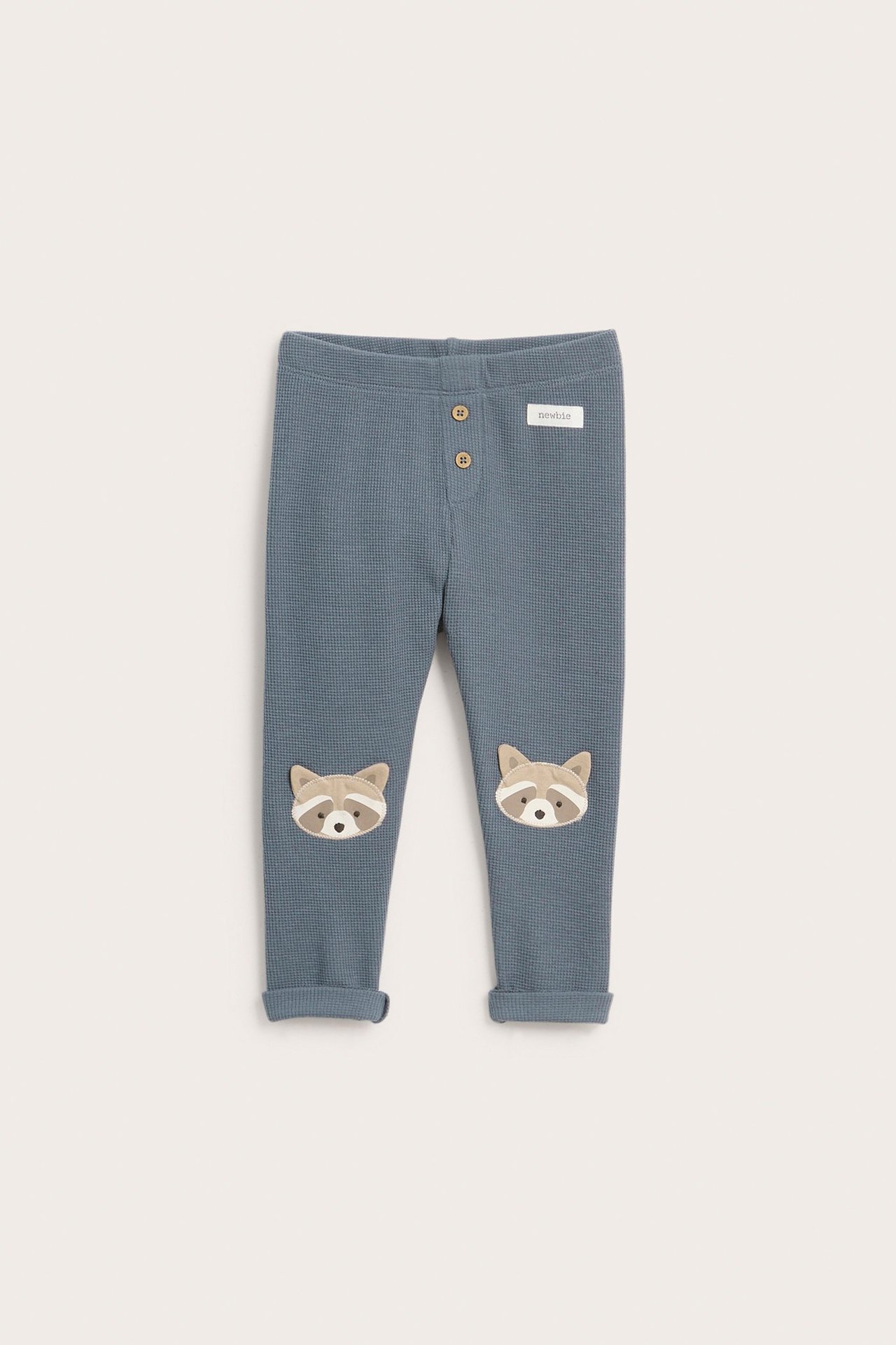 Vorderansicht blauer Waffelstrick-Baby-Leggings mit Zierknöpfen und Waschbär-Knieapplikationen.