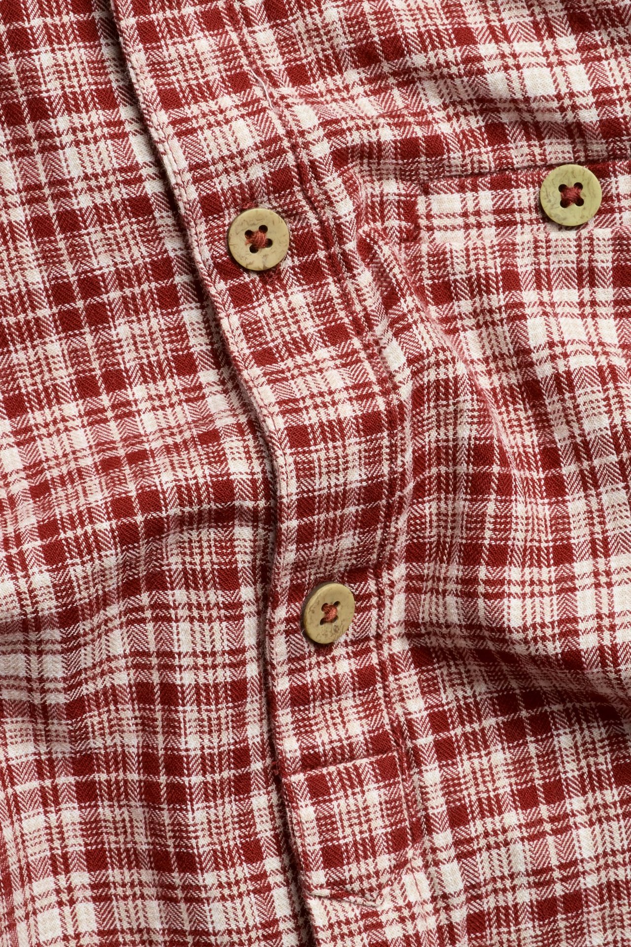 Nahaufnahme eines rot-weiß karierten Baumwoll-Shirtbodys mit hellbraunen Knöpfen.