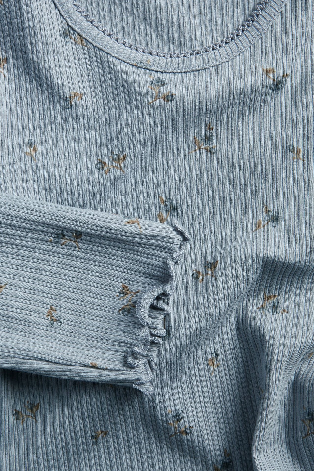 Nahaufnahme eines hellblauen gerippten Langarm-Baby-Tops mit Blumenmuster und Picot-Besatz.
