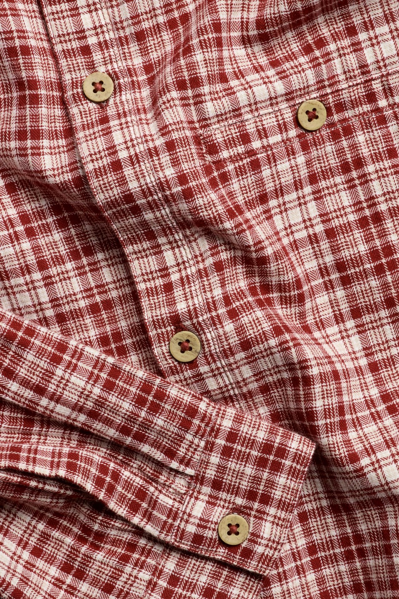 Close-up of a red and white checkered long-sleeved cotton shirt with wooden buttons.