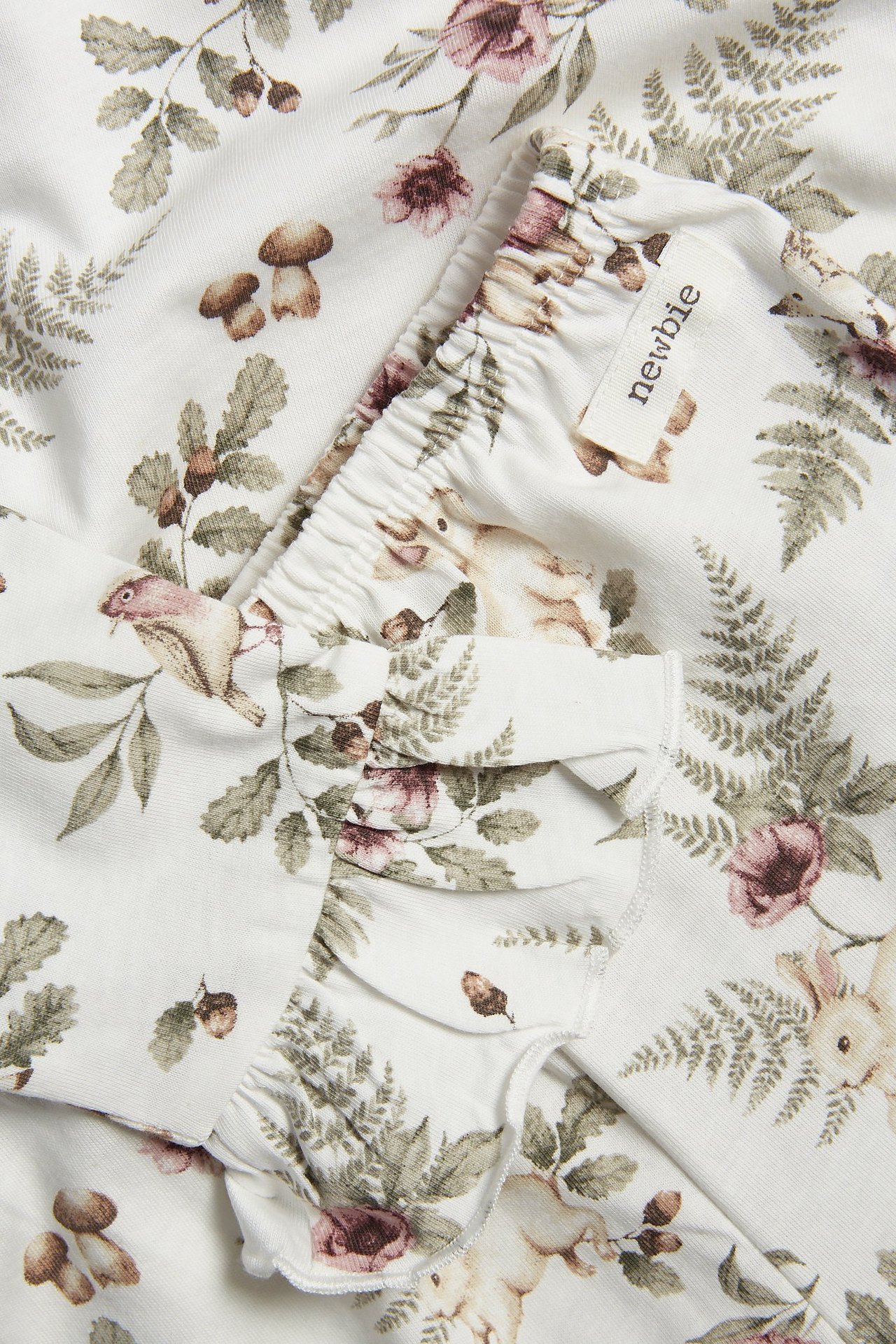Nahaufnahme eines cremeweißen Kinder-Baumwollpyjamas mit Blumen- und Waldtiermuster, Rüschen und Gummizug.