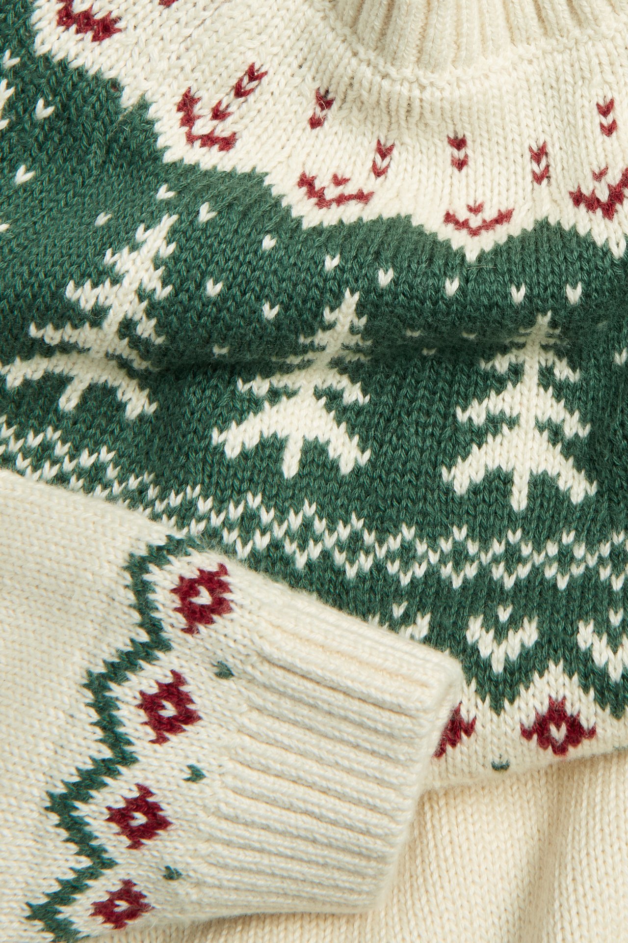 Nahaufnahme eines cremefarbenen Strickpullovers mit grün-rotem Jacquard-Tannenbaum-Muster.