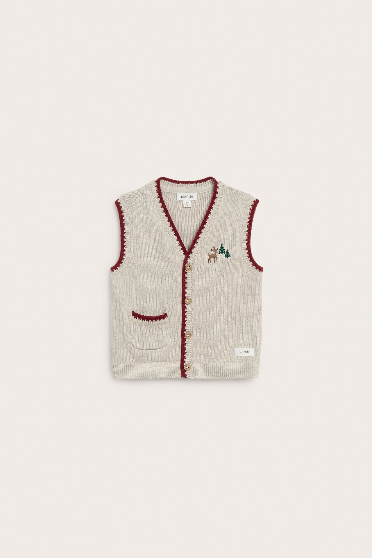 Front view of a kid's beige melange knitted vest with buttons, red trim, pocket, and reindeer embroidery.