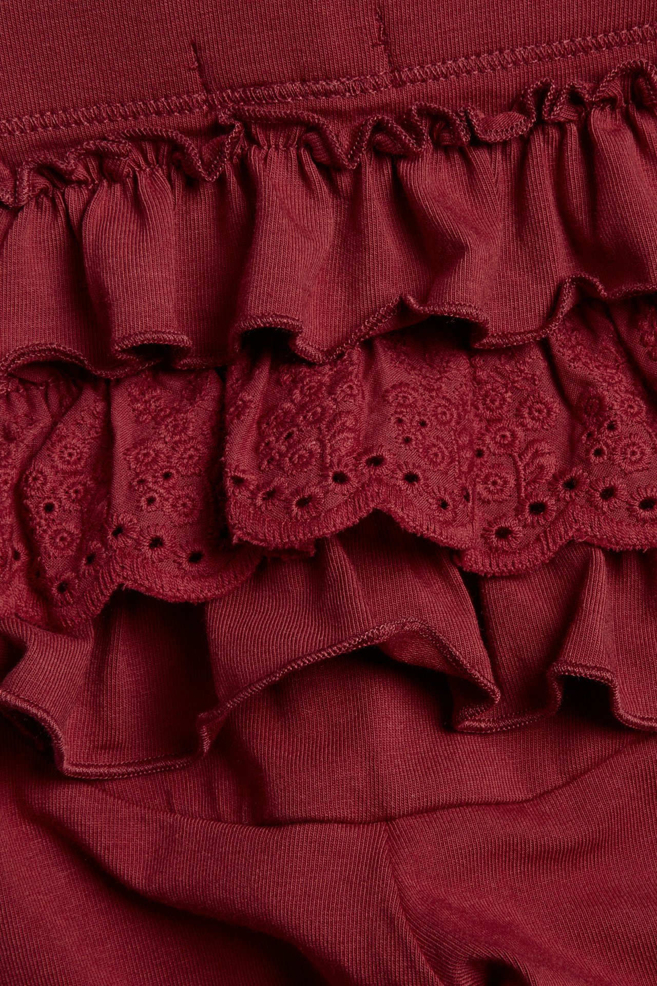 Nahaufnahme von dunkelroten Kinderleggings mit Gummibund, mehreren Rüschen und einer Spitze Schicht.