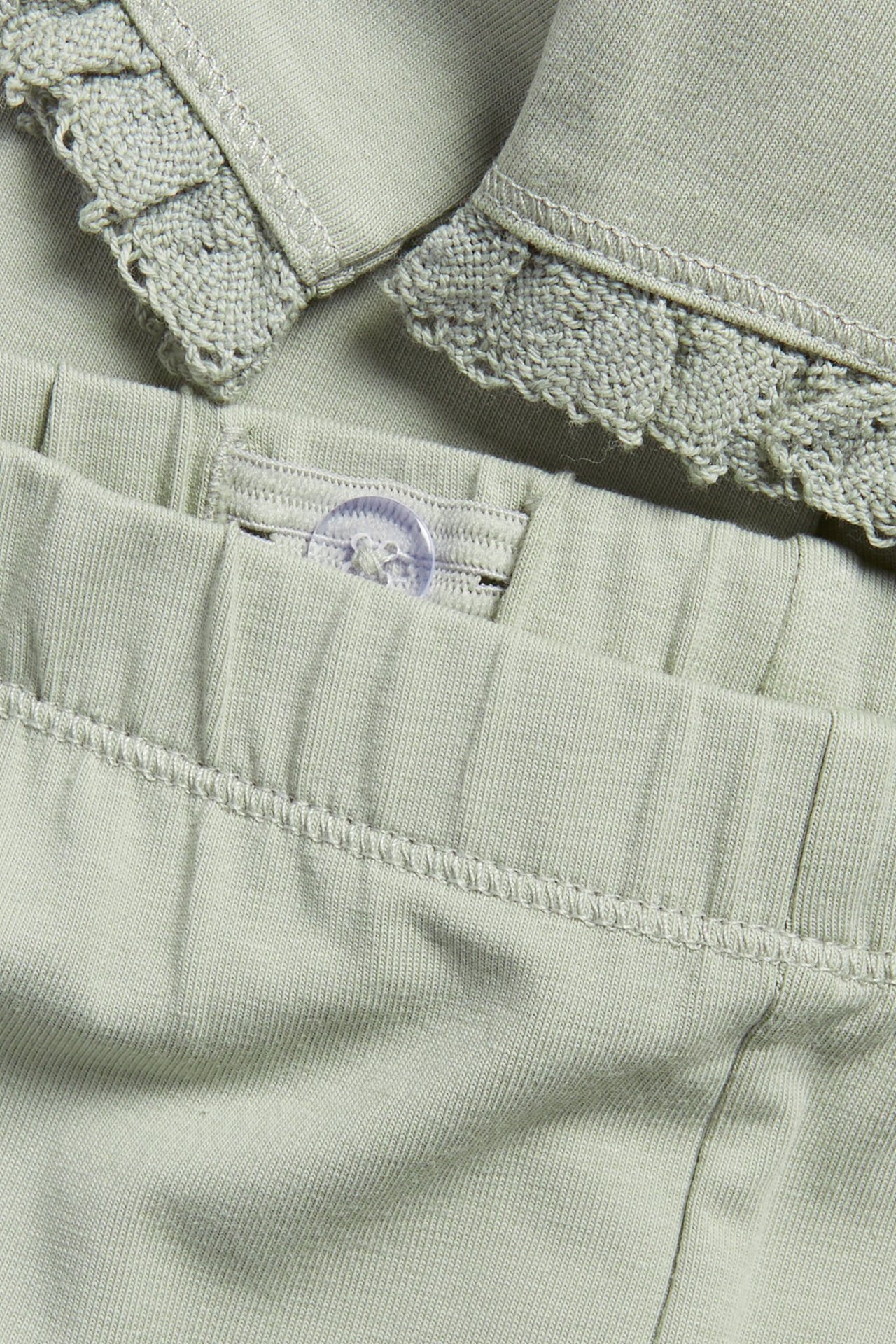 Close-up view of green cotton leggings with an adjustable elastic waistband and lace ruffle detail.