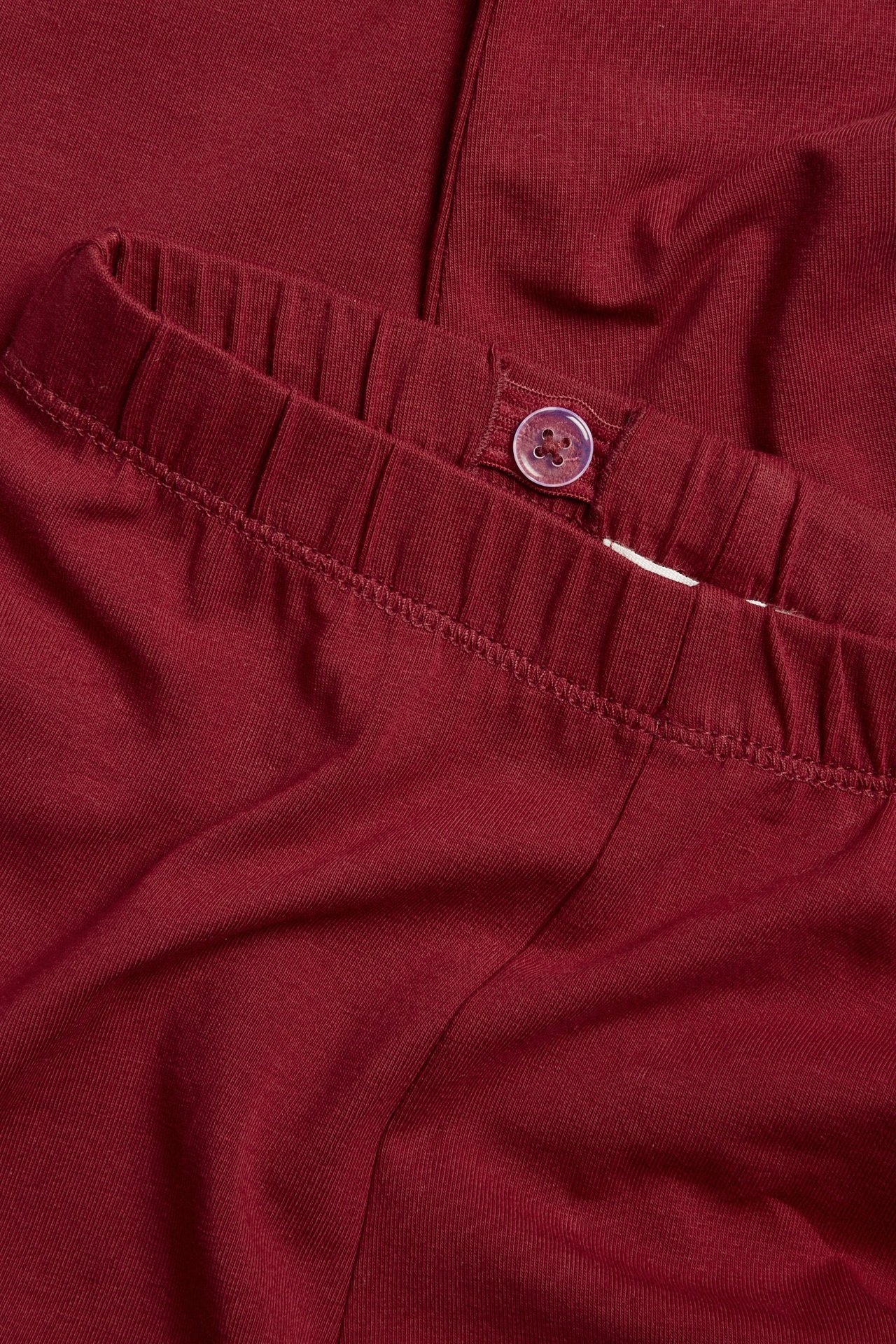 Close-up of kid's red cotton jersey leggings showing the adjustable elastic waistband with a button.
