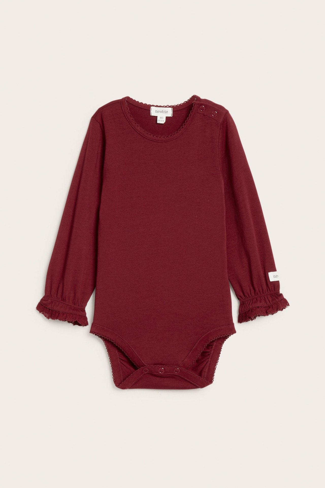 Front view of a red long-sleeved baby bodysuit with picot trim, lace cuffs, and snap buttons.