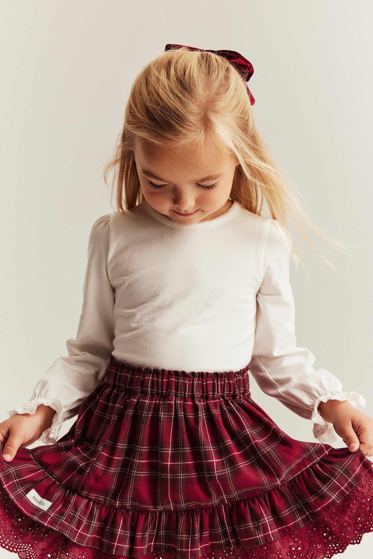 Young girl in white long-sleeve top with lace trim, red plaid ruffled skirt