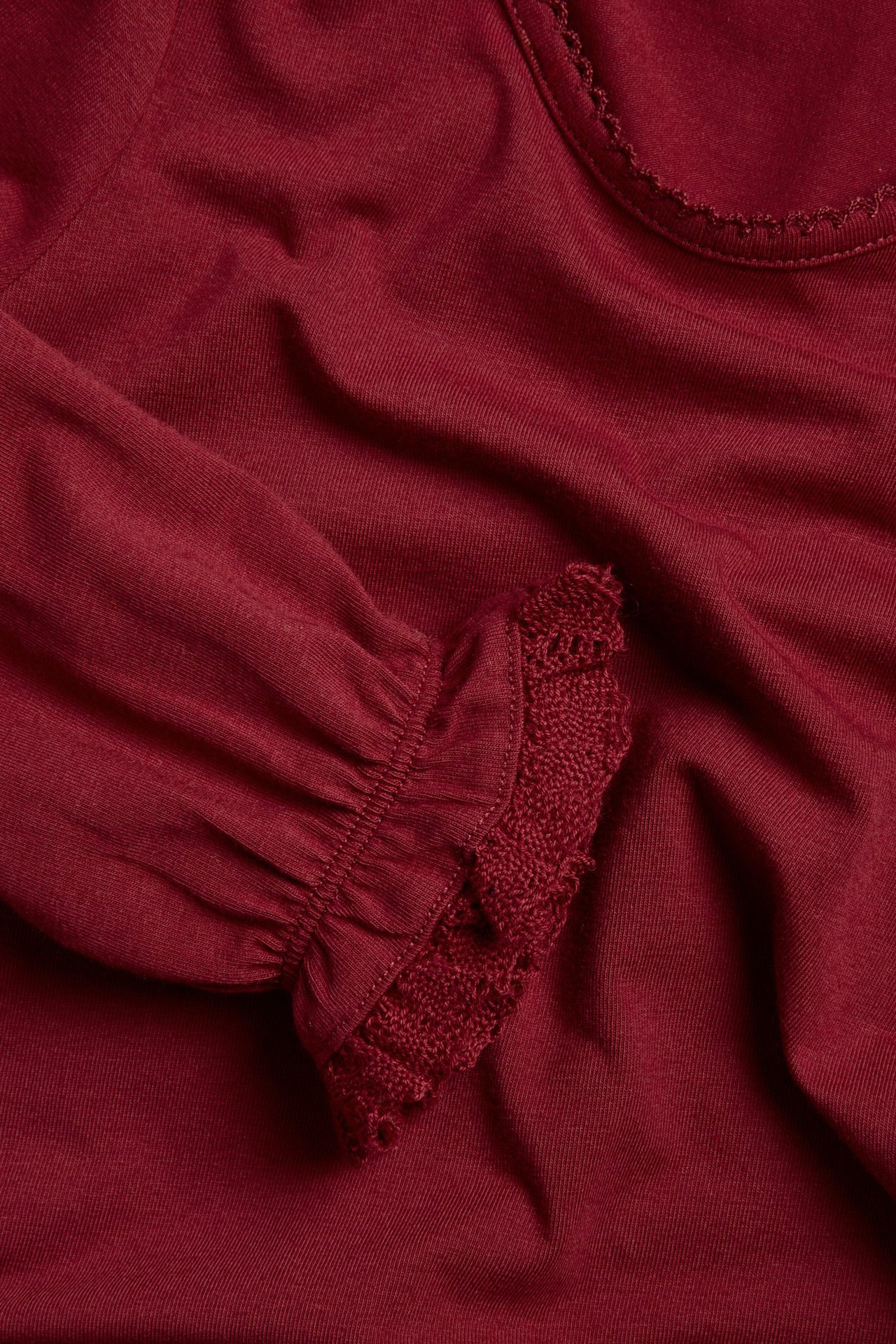 Close-up of a red long-sleeved cotton top with picot neckline and lace-trimmed elastic cuffs.