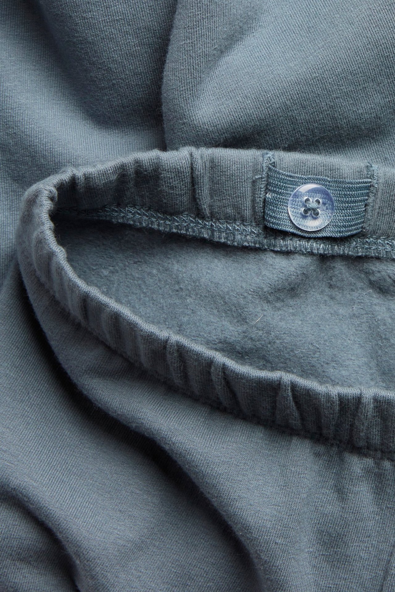 Nahaufnahme blauer Leggings mit elastischem Bund und verstellbarem Knopf, zeigt die gebürstete Innenseite.