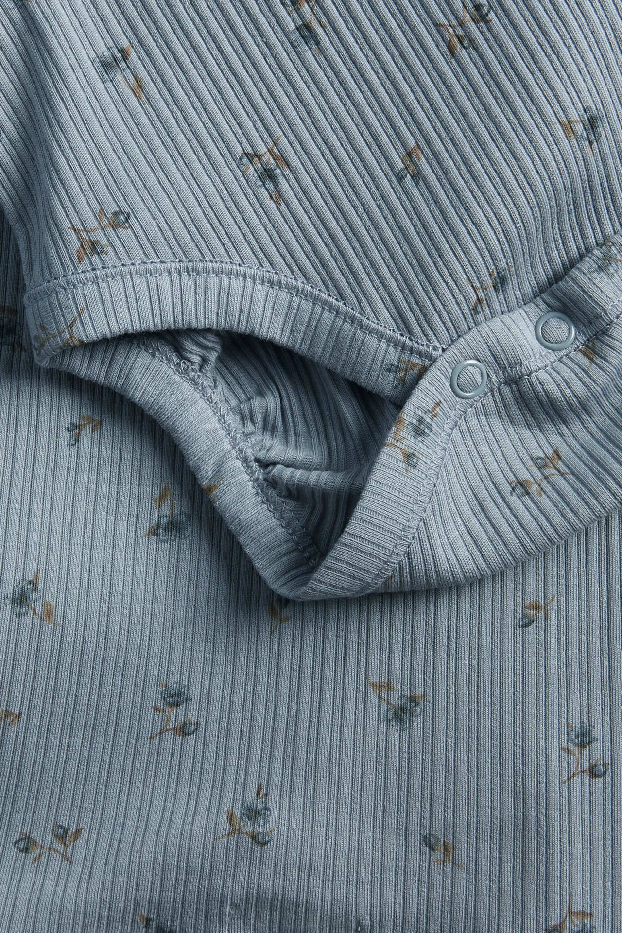 Nahaufnahme eines hellblauen gerippten Baby-Langarmbodys mit Blumenmuster und Druckknöpfen.