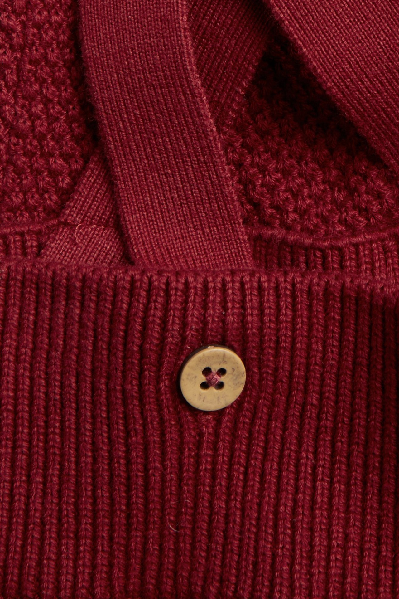 Nahaufnahme von roten gestrickten Baby-Latzhosen, strukturiert, mit gerippter Taille, verstellbaren Trägern, Holzknopf.