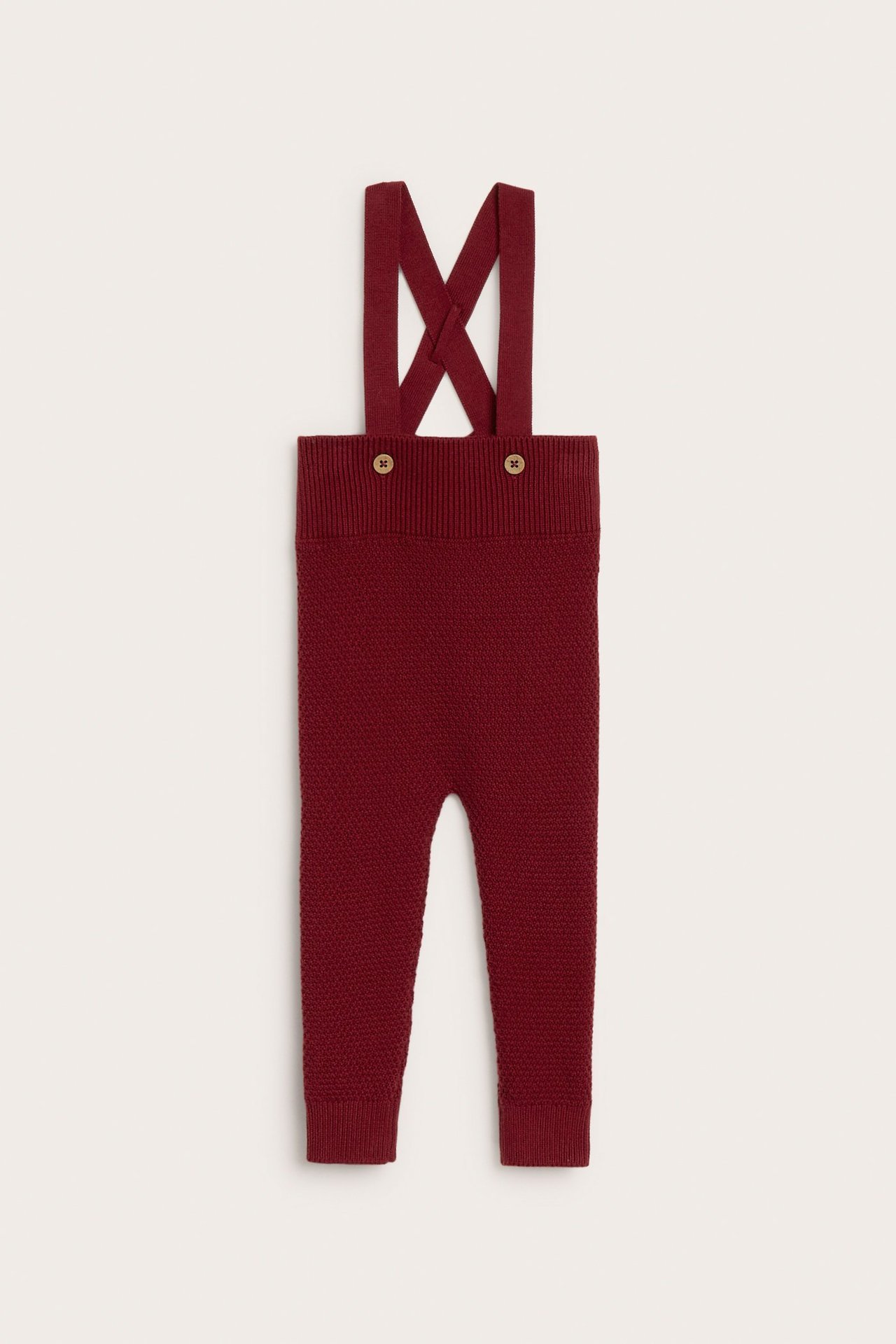 Front view of baby's deep red structured knit dungarees with adjustable straps and wooden buttons.