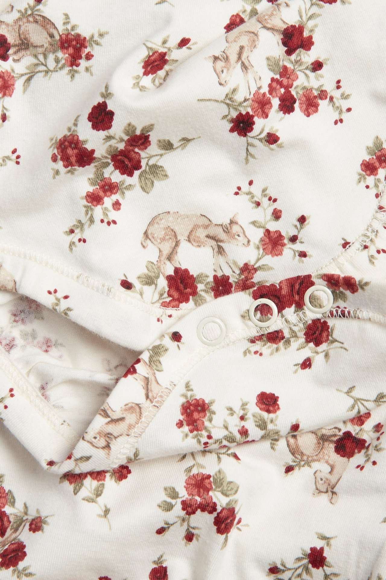 Close-up of an off-white baby bodysuit with a floral and fawn print, featuring snap buttons.