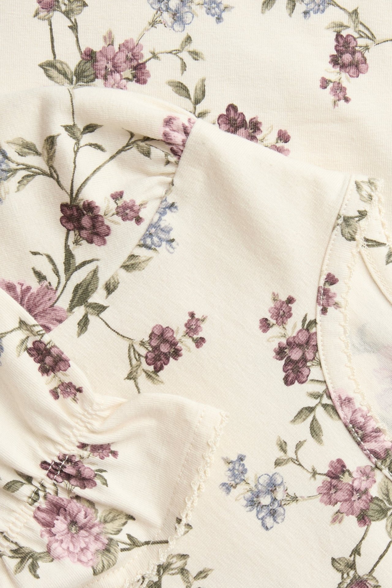 Nahaufnahme eines hellbeigen Blusentops mit lila und blauen Blumen, Puffärmeln und Picot-Kanten.