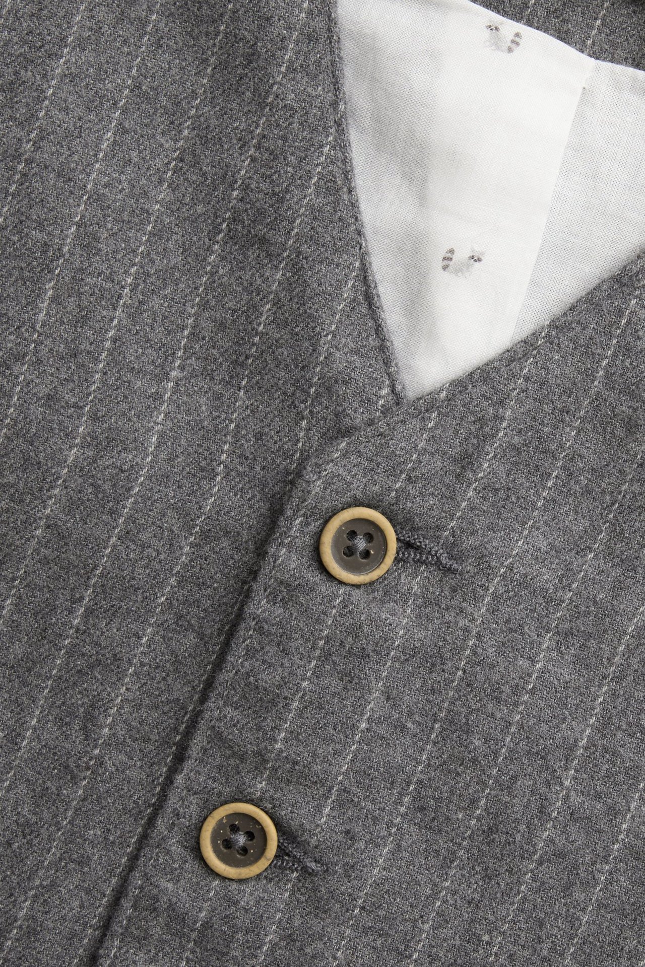 Nahaufnahme einer graumelierten Nadelstreifen-Webweste mit zwei geknöpften Knöpfen und weißem gemustertem Baumwollfutter.