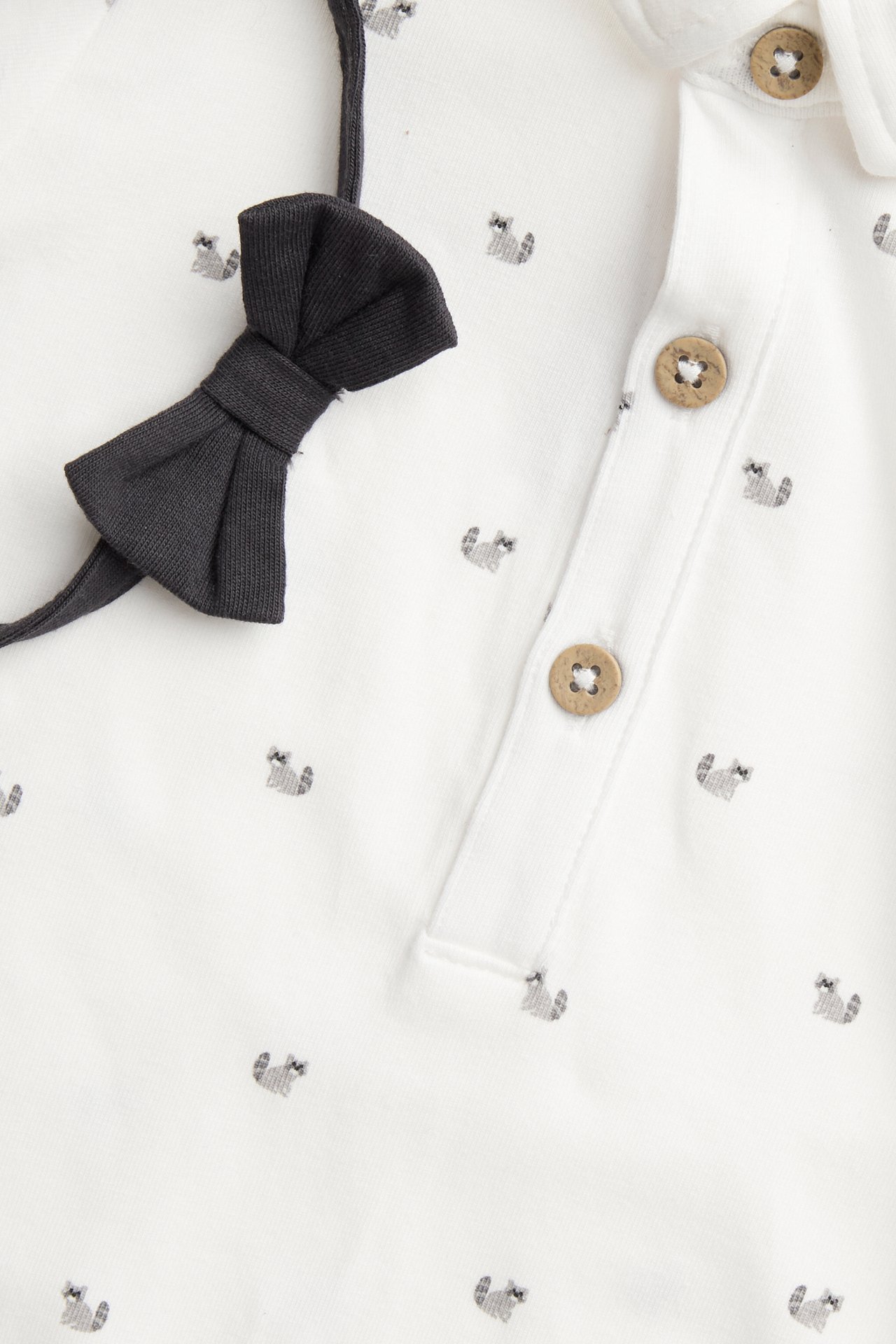 Close-up of an off-white baby bodysuit with animal print, button placket, and a black detachable bow tie.