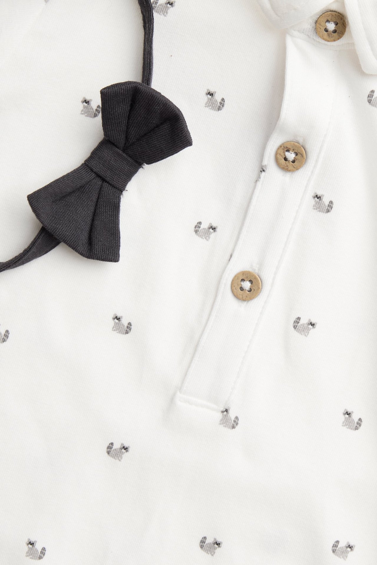 Nahaufnahme eines cremefarbenen Baby-Bodys mit Tiermuster, Knopfleiste und einer schwarzen abnehmbaren Fliege.