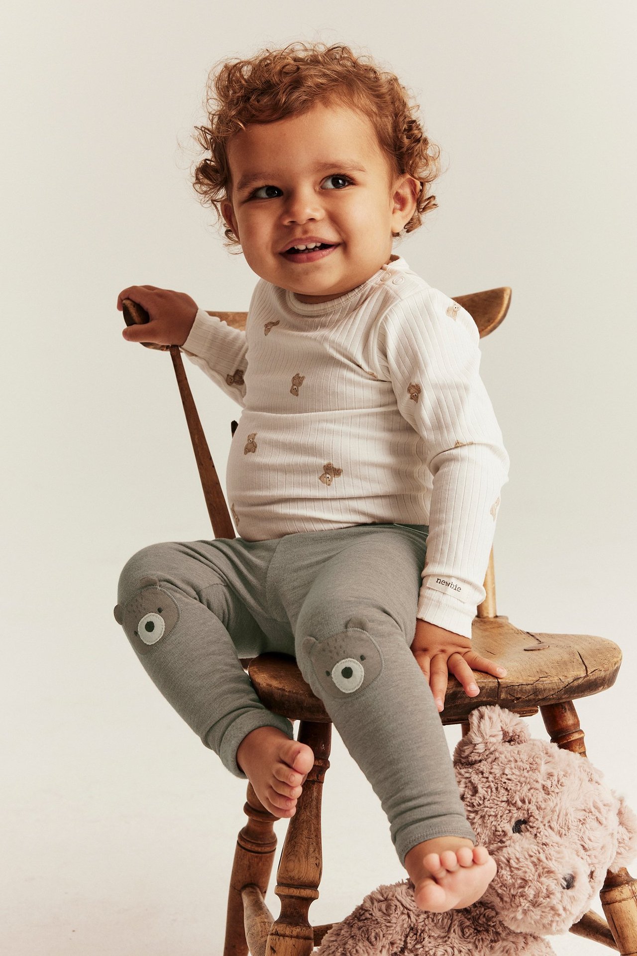 Front view of a baby wearing grey leggings with bear-face knee appliqués and a white ribbed long-sleeve top.