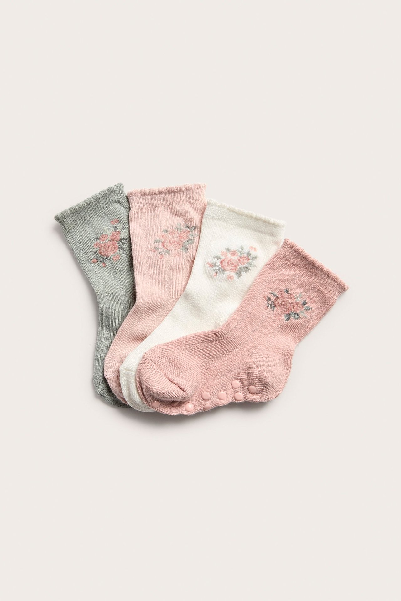 Draufsicht auf vier strukturierte Babysocken: hellrosa, weiß, grau, rosé, mit Blumenstickerei. Ein Paar hat Antirutsch-Noppen.
