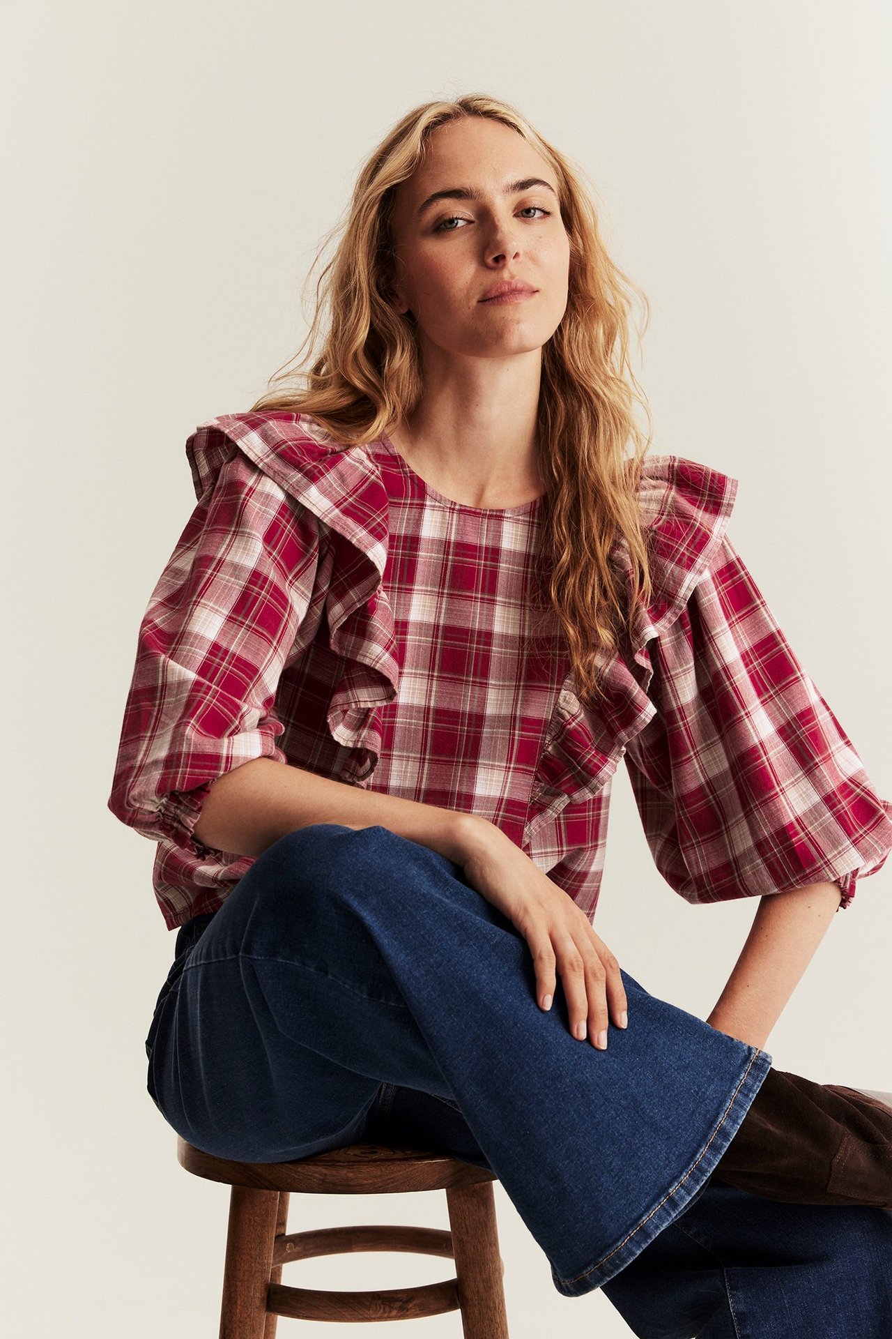 Frontansicht einer Frau in rot-weiß karierter Baumwoll-Rüschenbluse und blauen Jeans.