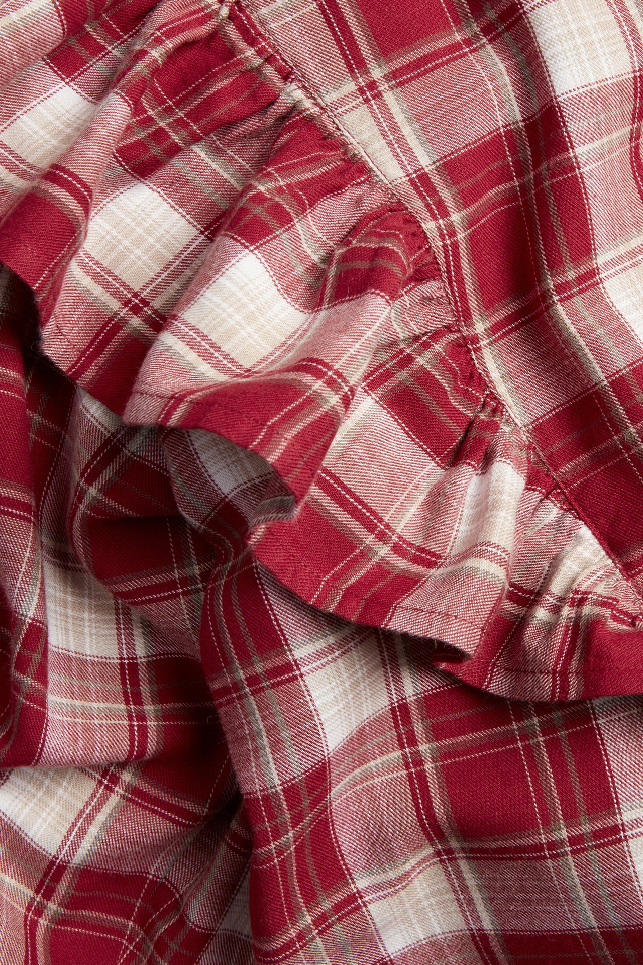 Nahaufnahme einer rot-beig-weiß karierten Baumwollbluse mit sichtbaren Rüschen und Stoffstruktur.