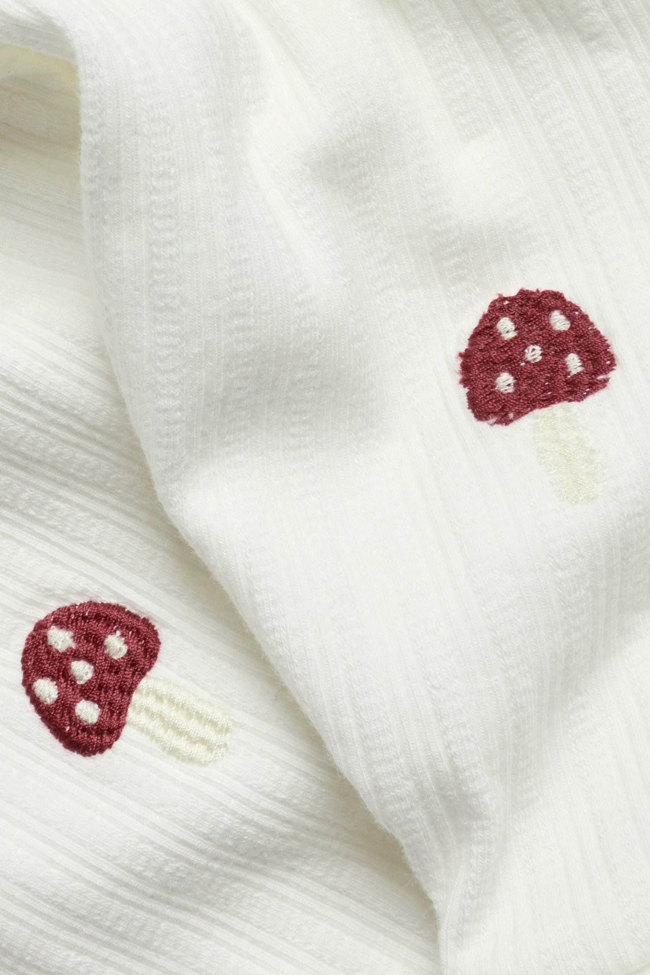 Close-up of off-white ribbed leggings with red mushroom embroidery.