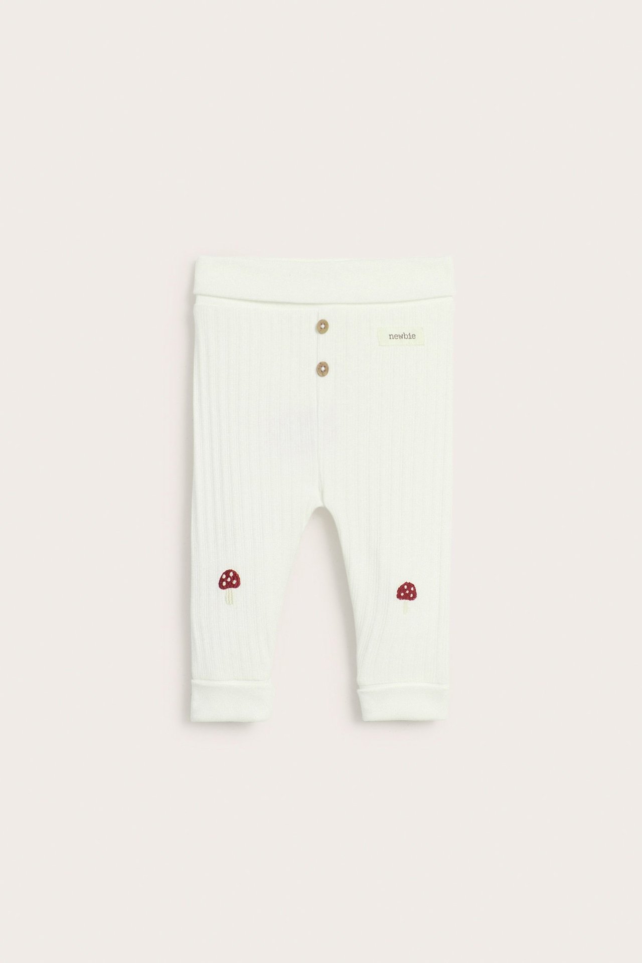 Front view of off-white ribbed baby leggings with mushroom embroidery on knees and decorative buttons.