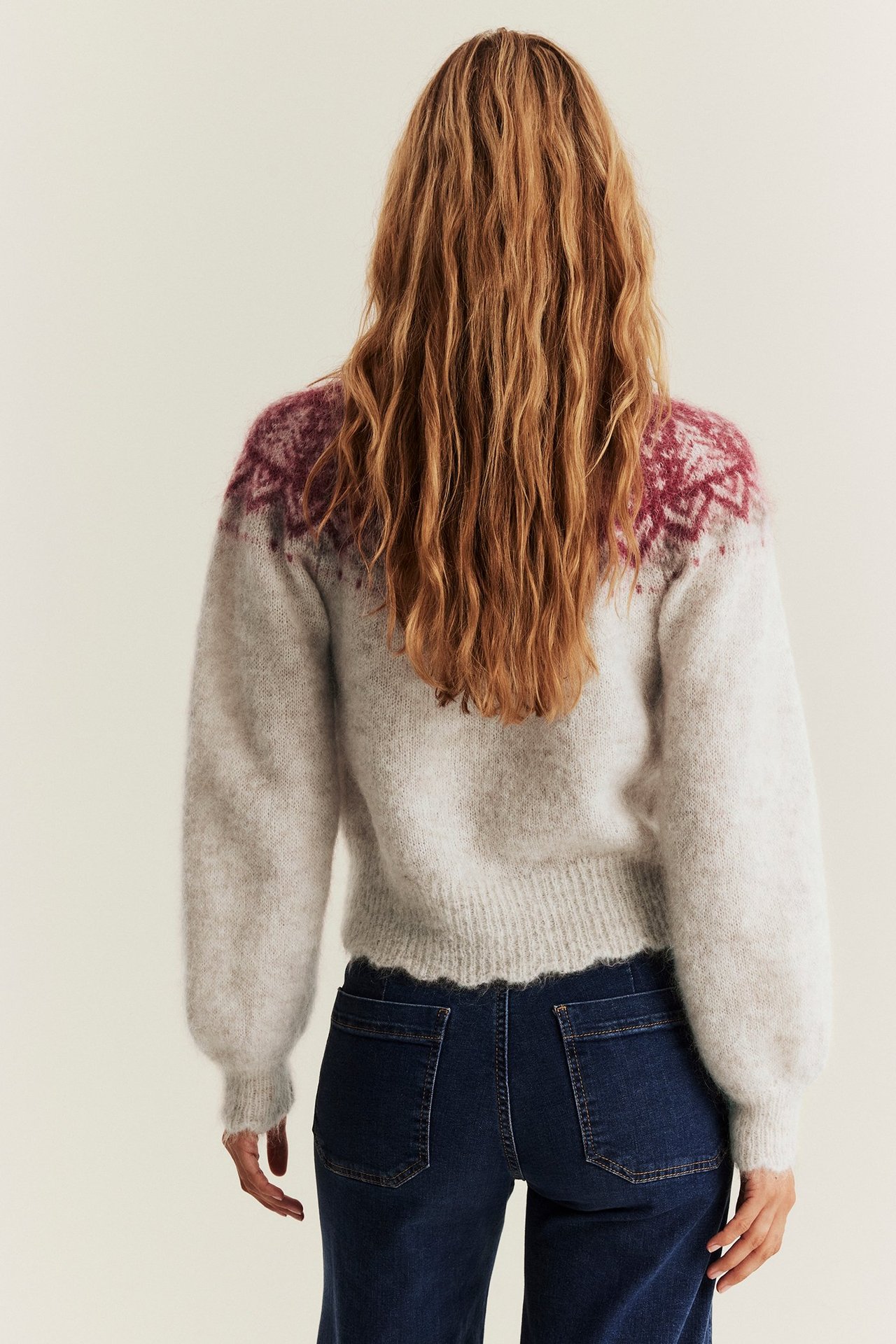 Back view of woman wearing a beige melange jacquard wool-blend cardigan and dark blue jeans.