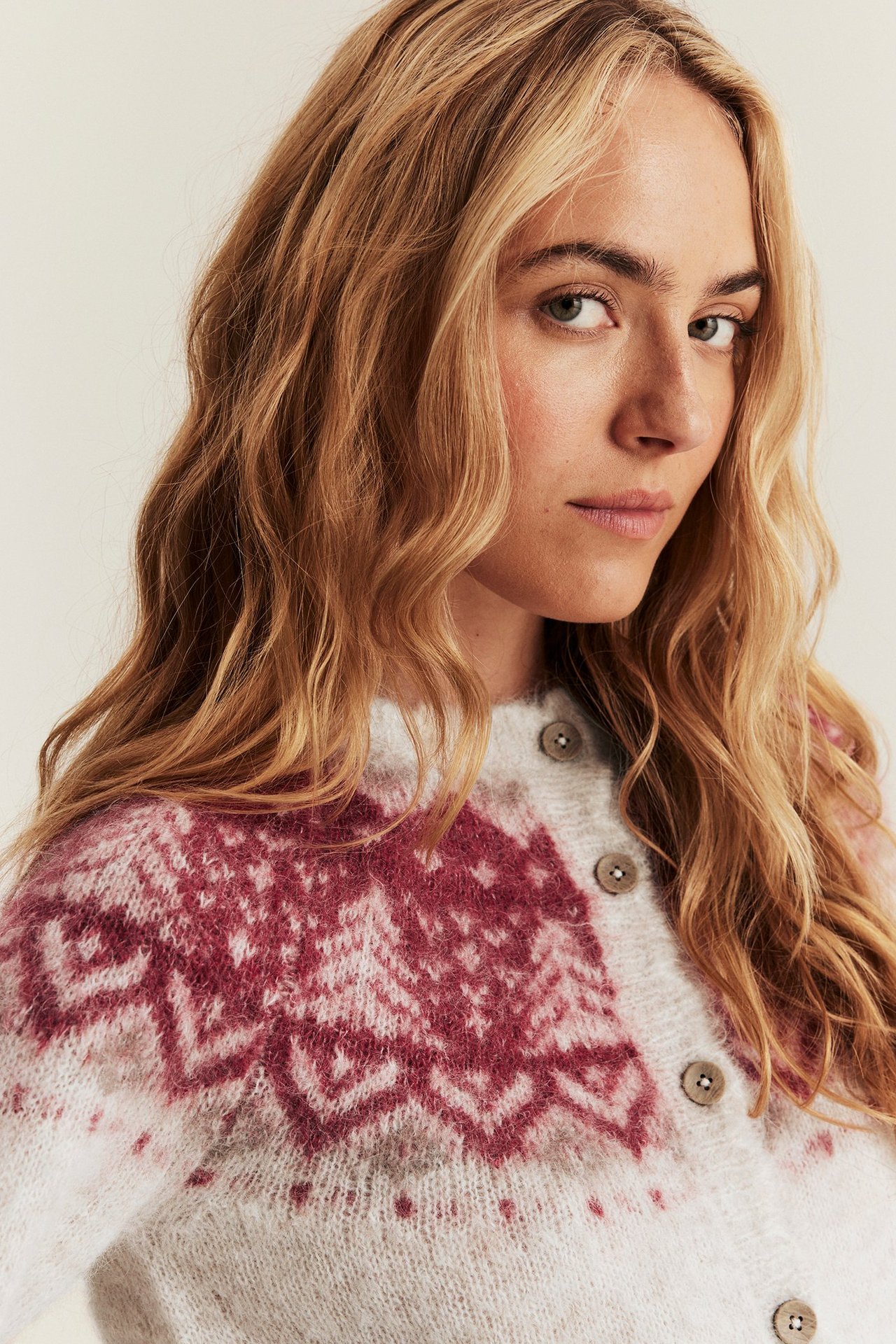 Close-up, front view: Woman in light beige melange wool blend jacquard cardigan with red patterns and buttons.