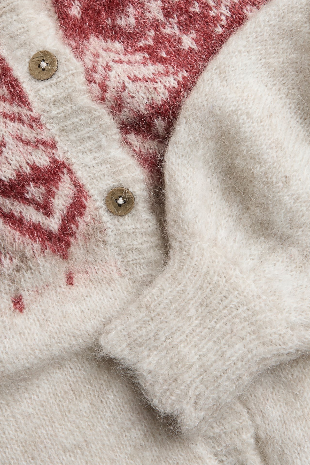 Close-up of a beige melange knitted cardigan with red jacquard pattern and brown buttons.