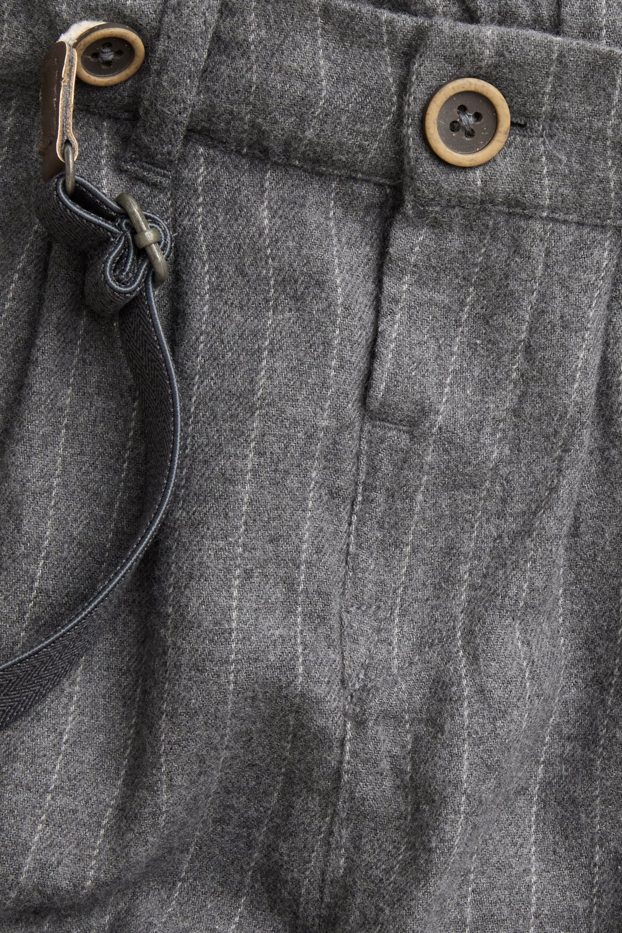 Close-up of grey pinstriped woven pants with a brown button and a dark suspender strap.