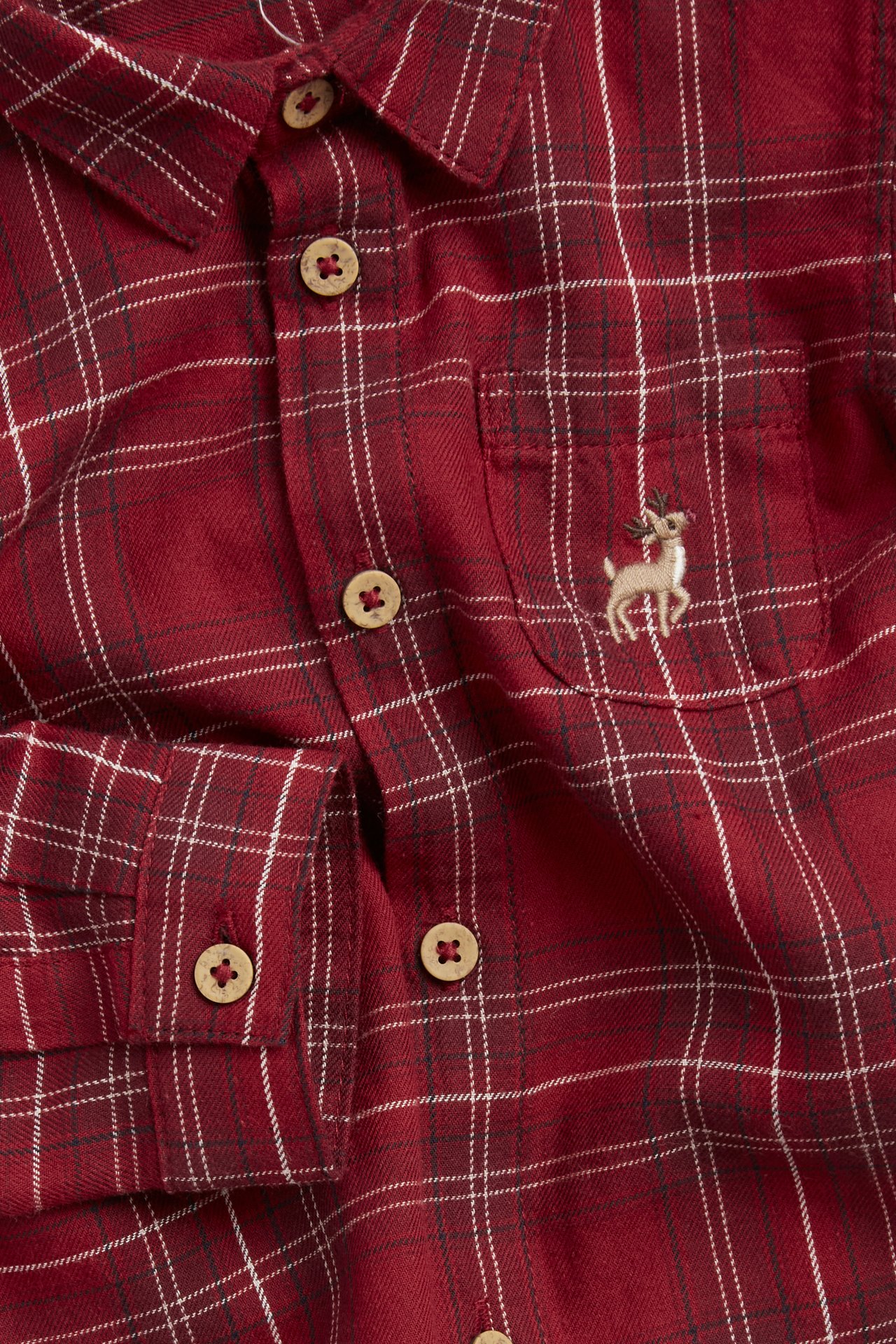 Close-up of a red plaid cotton shirt with wooden buttons and a deer embroidery on the chest pocket.