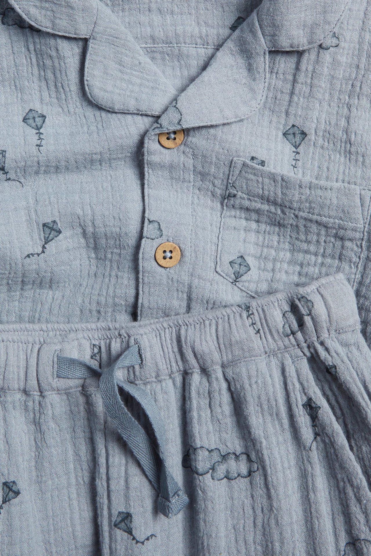 Nahaufnahme eines hellblauen Baumwollpyjamas mit Drachenmuster. Hemd mit Kragen, Knöpfen und Hose mit Kordelzug.