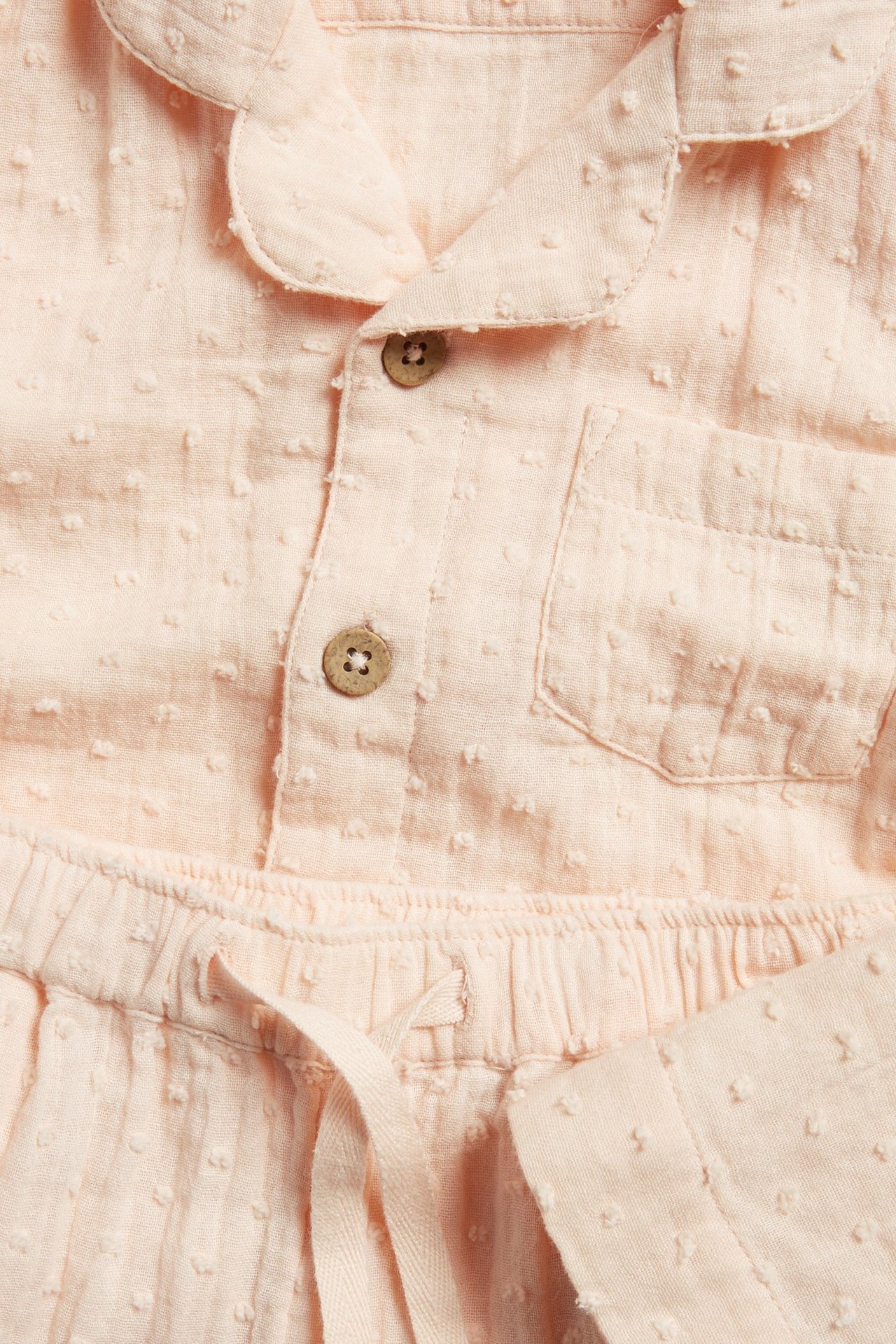 Close-up of a light orange dotted cotton pajama set, with a collared shirt and drawstring pants.