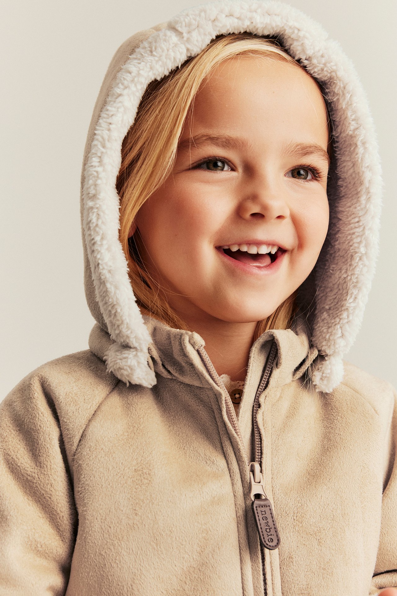 Close-up front view of a kid wearing a beige shearling-look jacket with a pile-lined hood and zipper.