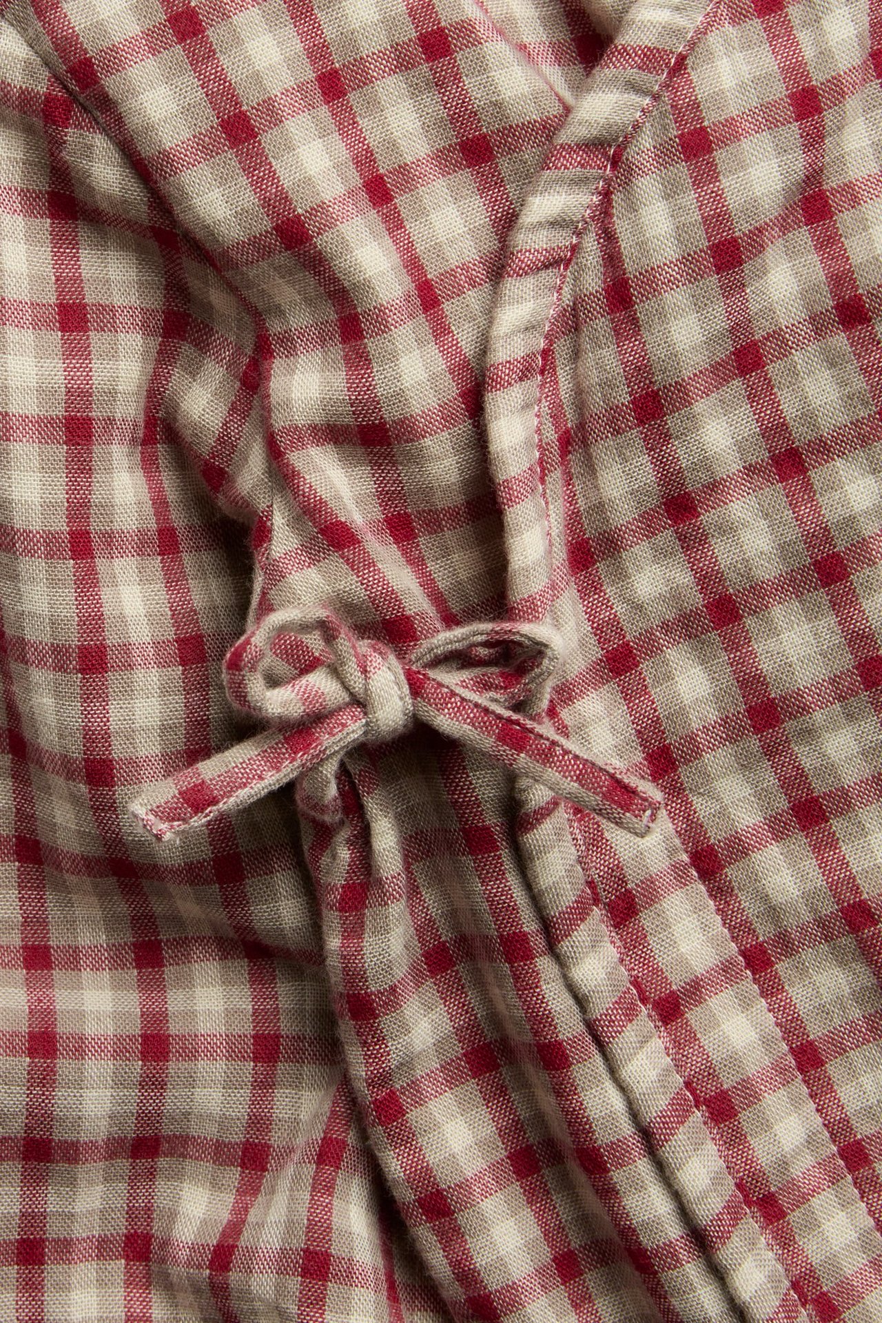 Nahaufnahme eines rot-beigekarierten Baumwoll-Wickelbodys für Babys mit Schleifenverschluss.