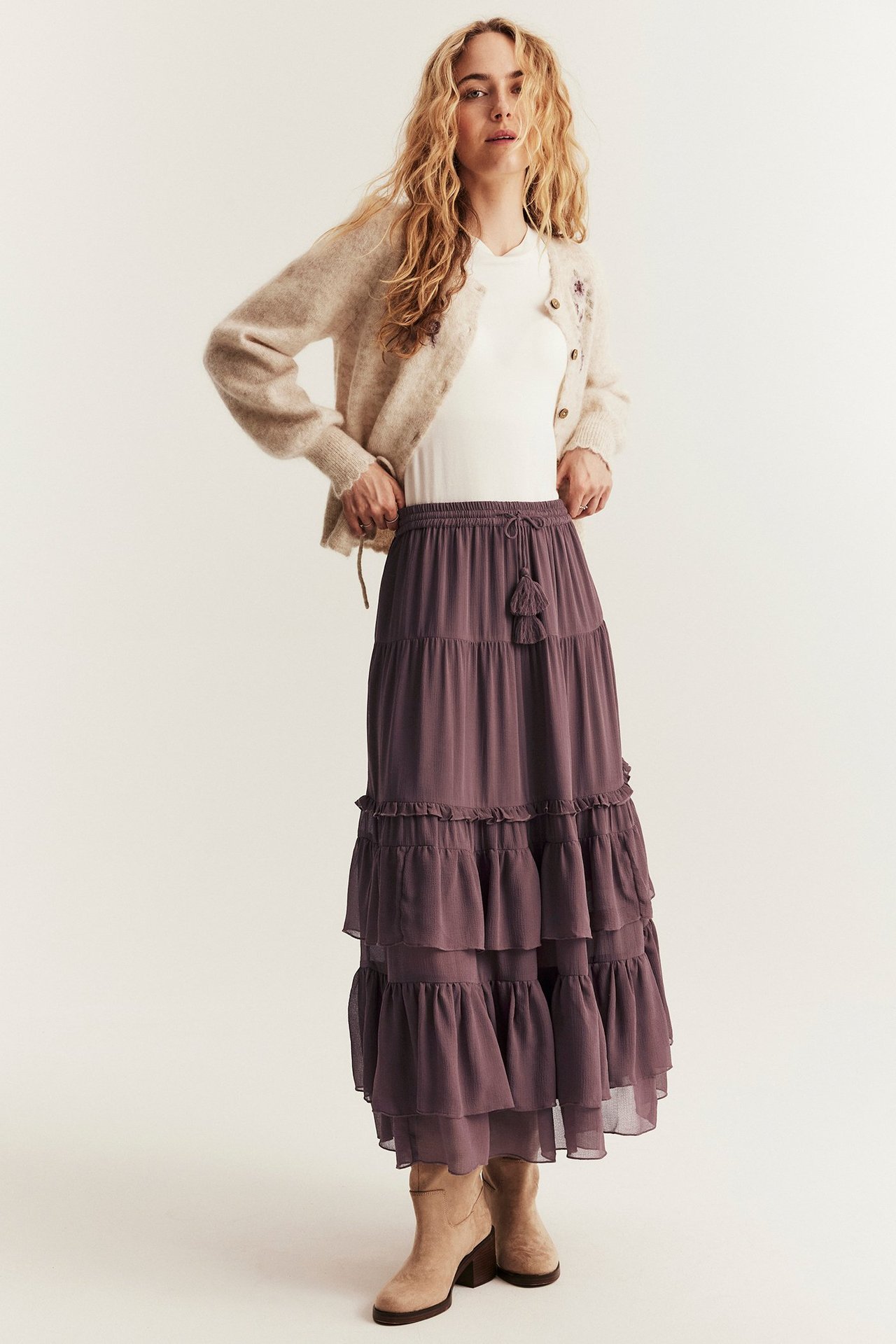 Woman in white T-shirt, beige cardigan, long lilac chiffon skirt with ruffles, front view.