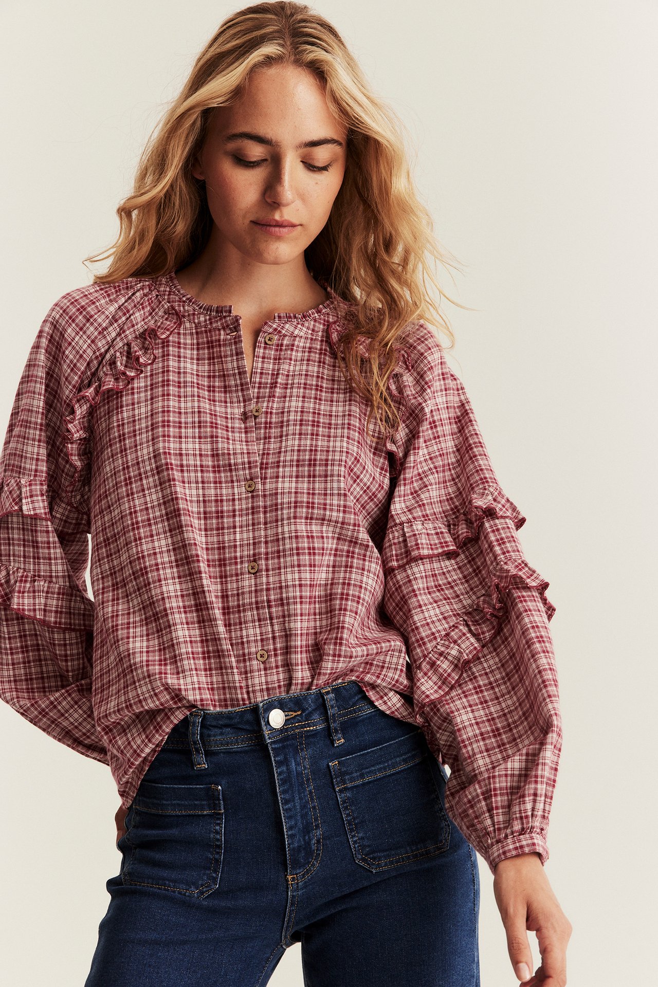 Front view of a woman wearing a red plaid cotton blouse with ruffles and dark blue jeans.