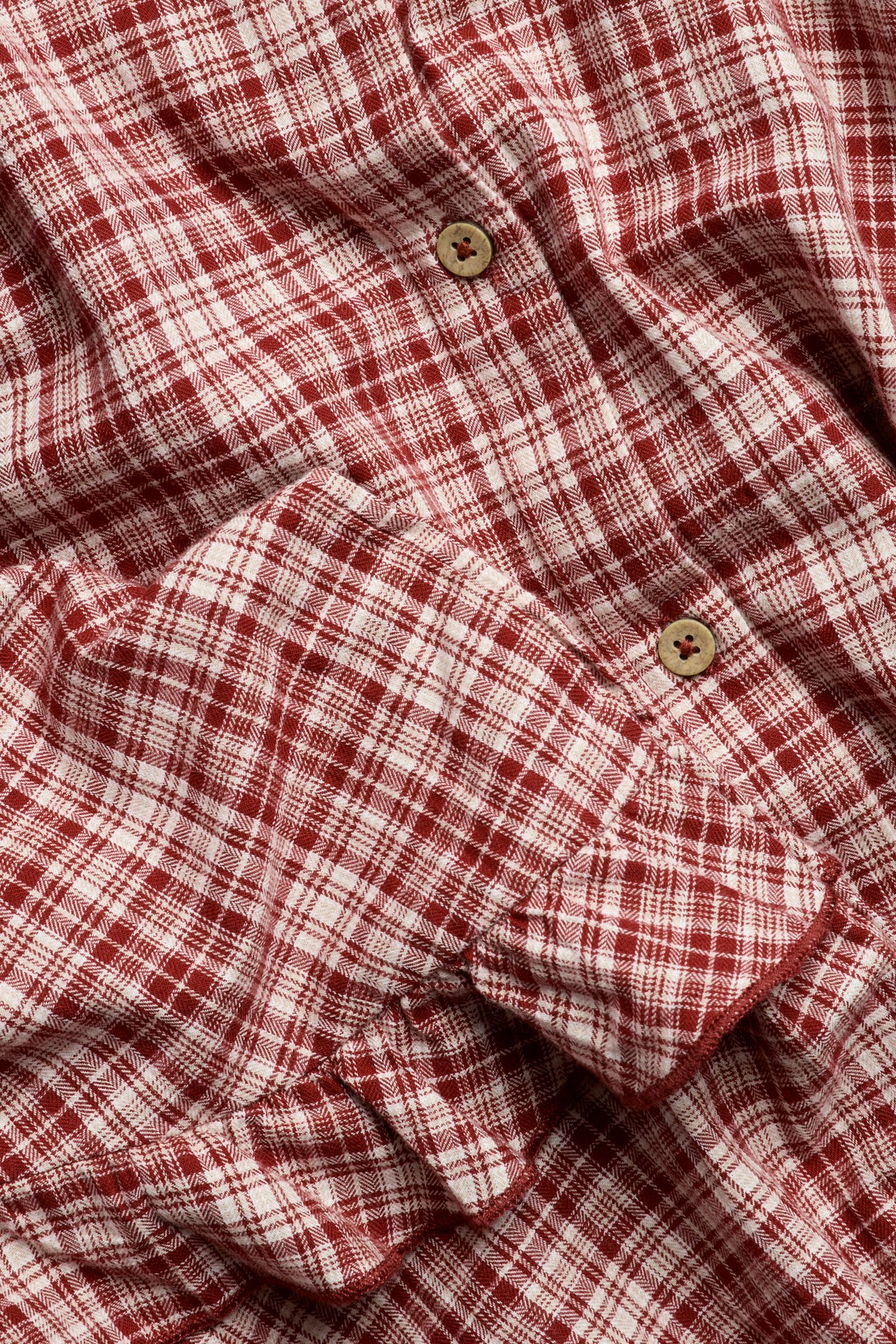 Close-up of a red and white plaid woven cotton blouse with wooden buttons and ruffles.