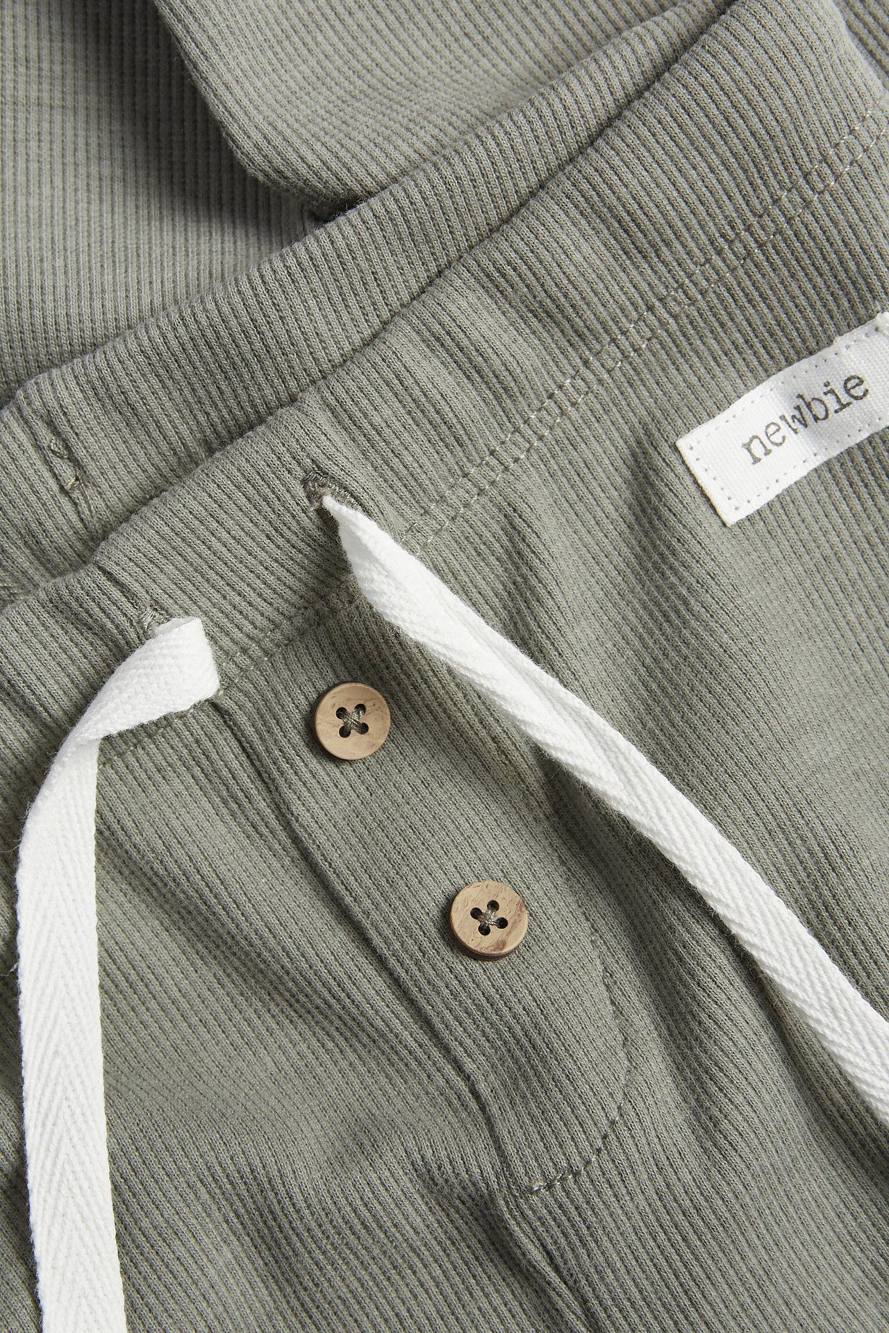 Close-up of dark green ribbed leggings with a white drawstring and two decorative wooden buttons on the waistband.