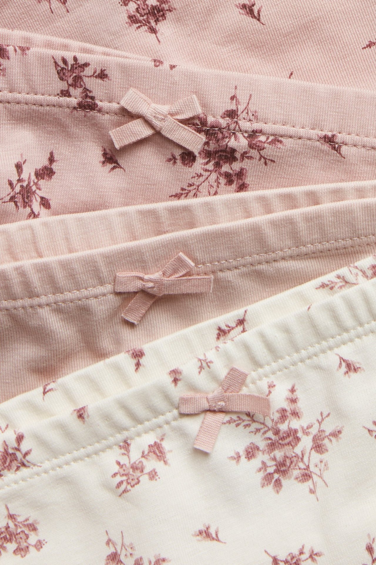 Nahaufnahme von drei Kinder-Jersey-Boxershorts: zwei rosa, eine cremefarben, alle geblümt mit kleinen rosa Schleifen.