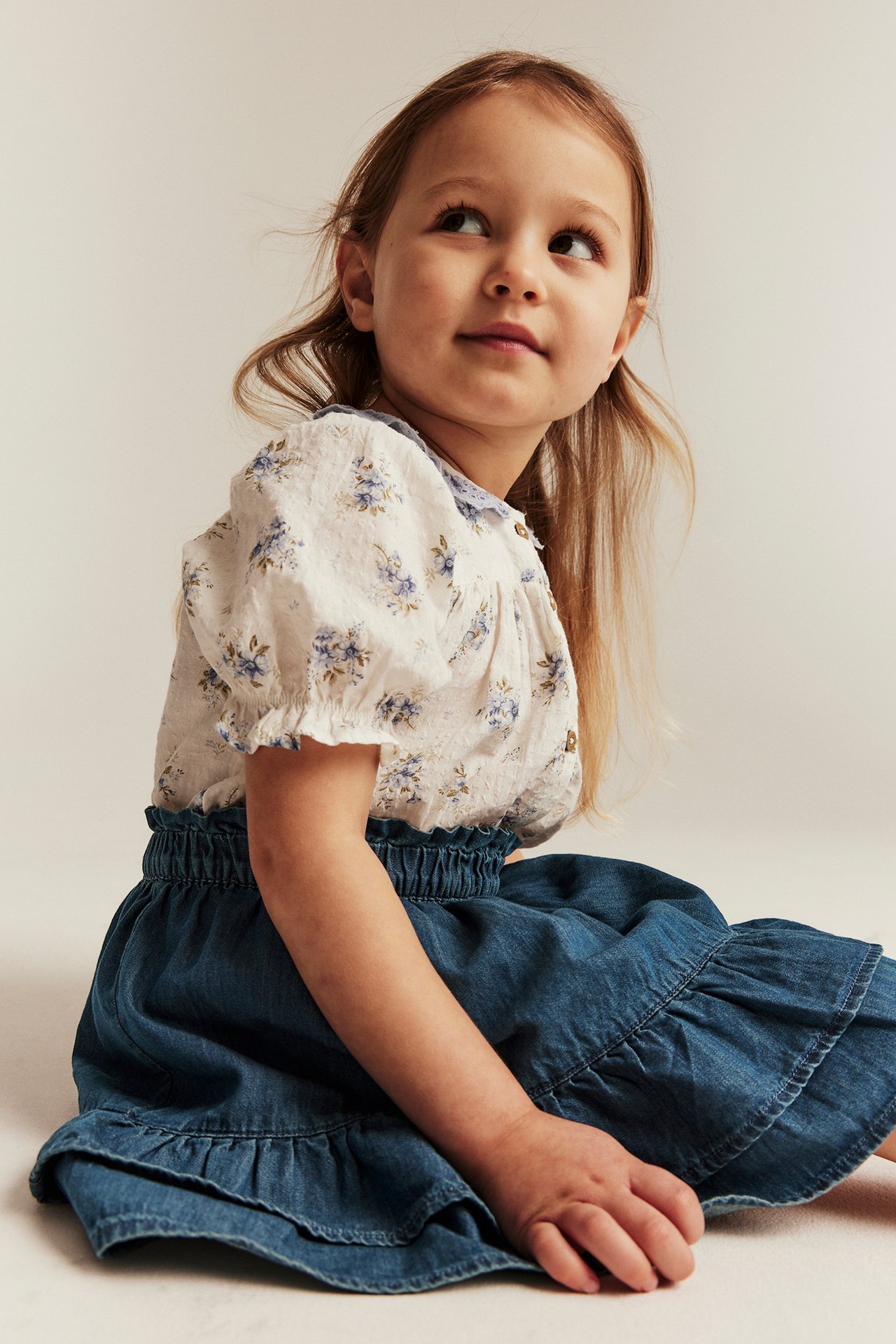 Close-up of a kid wearing a blue denim skirt with an elasticated waist and a white floral blouse.